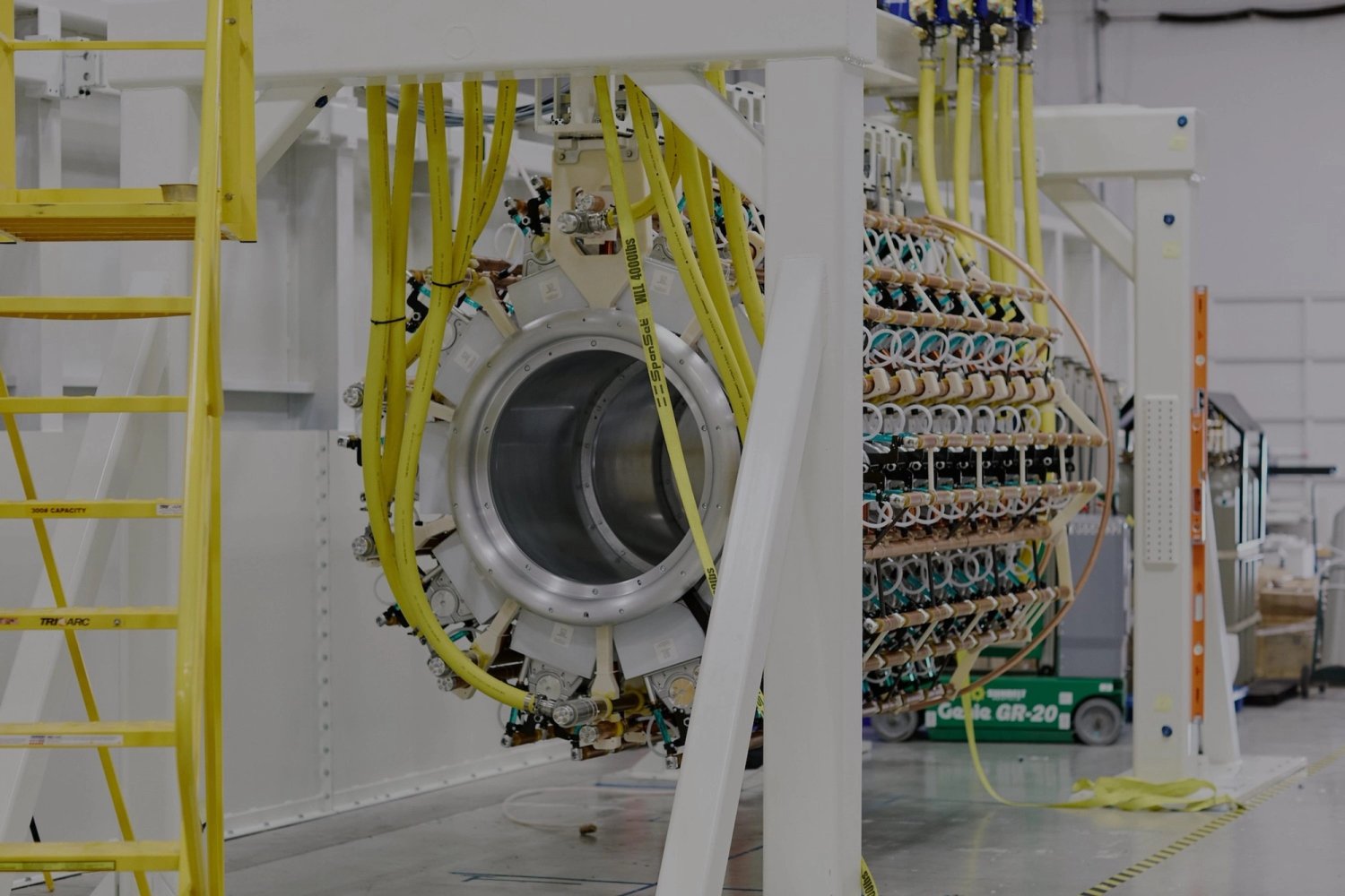 Pacific Fusion’s scaled pulser-module prototype: a cylindrical high-voltage assembly with copper components and yellow cables in a white steel frame.
