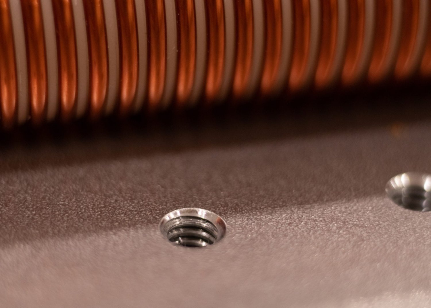 Close-up of fusion hardware showing a threaded hole in a textured metal plate, with copper wiring in the background.