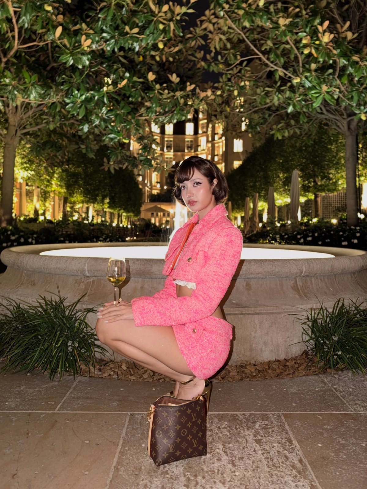 Lisa agachada no mesmo jardim, ao lado de uma bolsa marrom