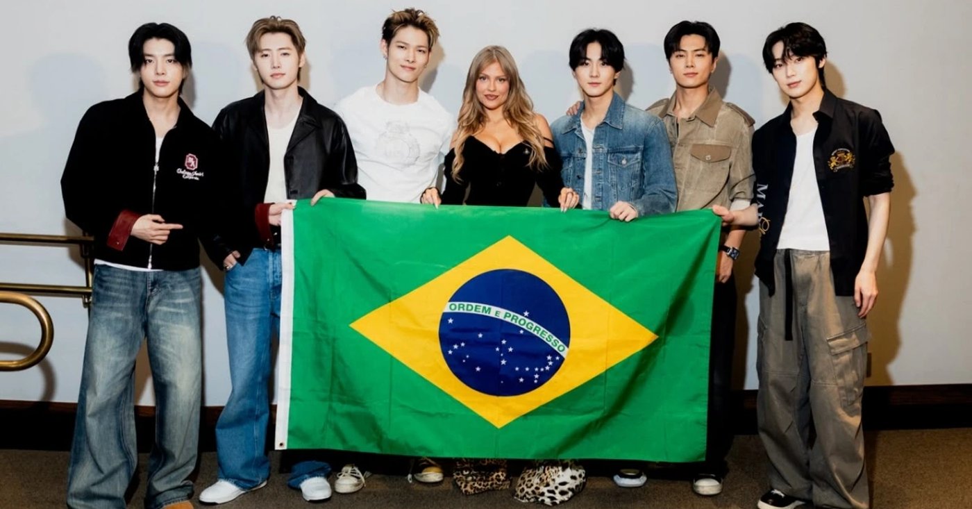 Luísa Sonza posa com os sete integrantes do ENHYPEN diante de uma bandeira do Brasil.