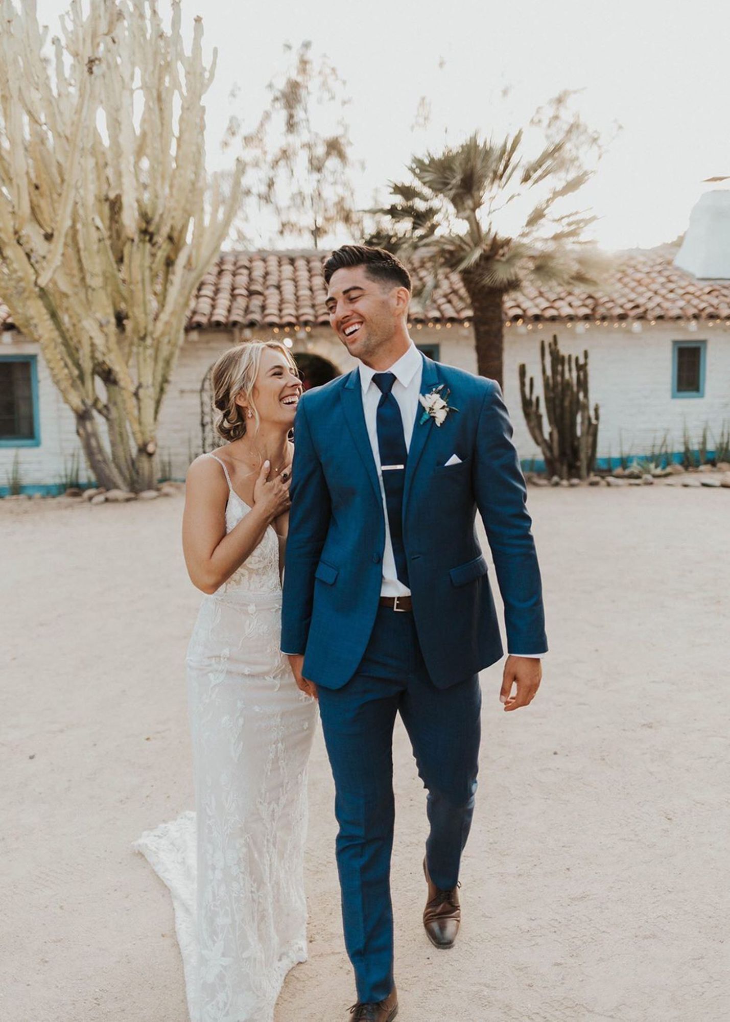 photo of groom wearing a blue suit laughing and holding hands with a bride in white wedding dress