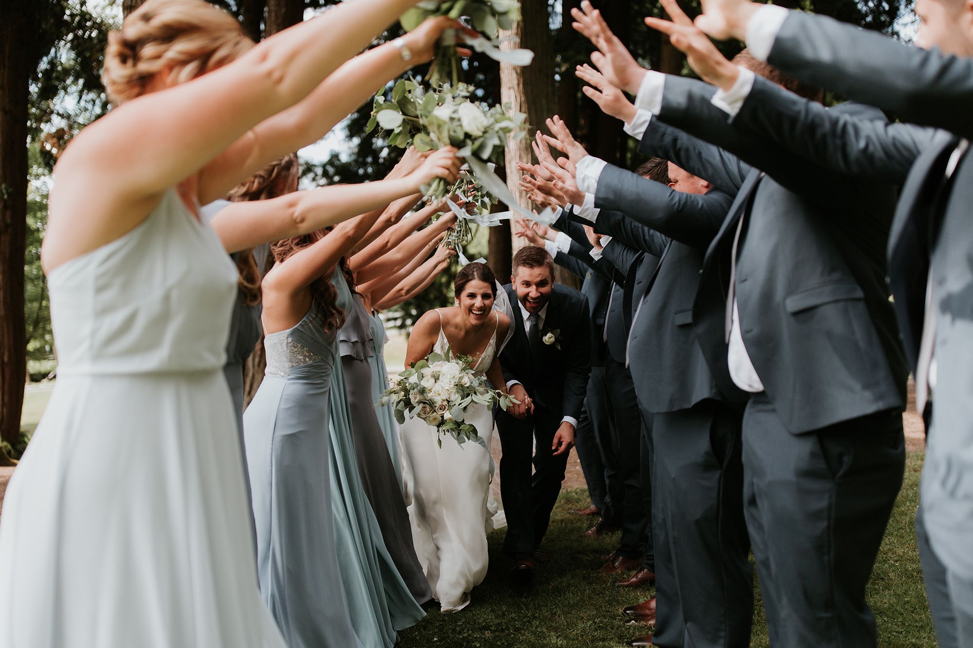 photo of groomsmen in gray suits and bridesmaids making a tunnel with their arms
