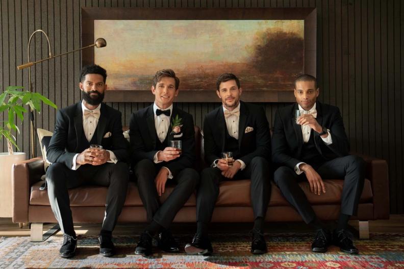 4 groomsmen in black tuxedos on a couch