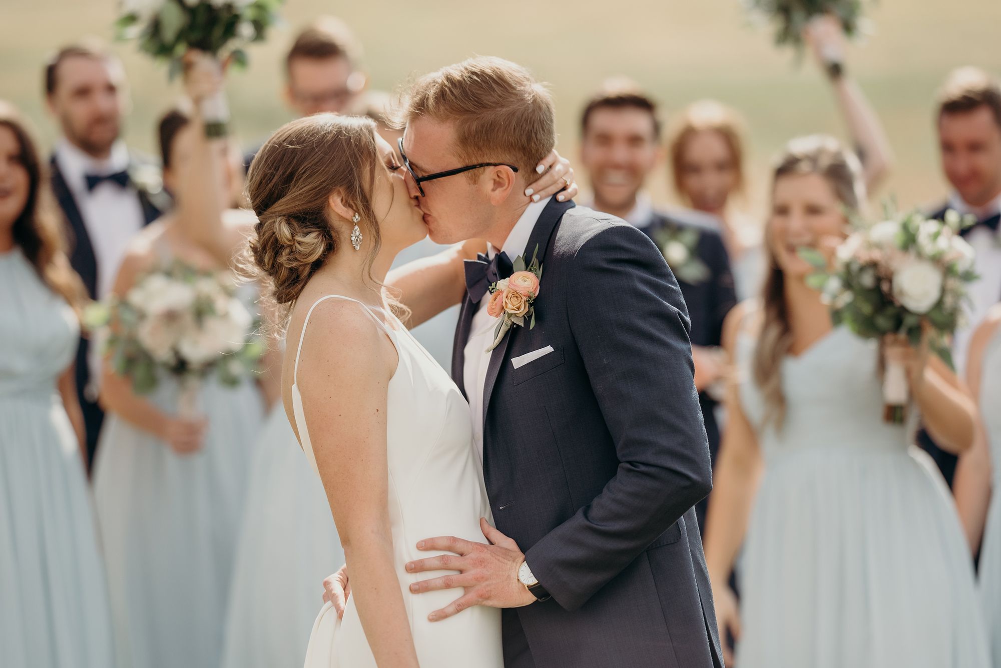 photo of a blonde groom in a blue suit kissing his bride during a wedding ceremony