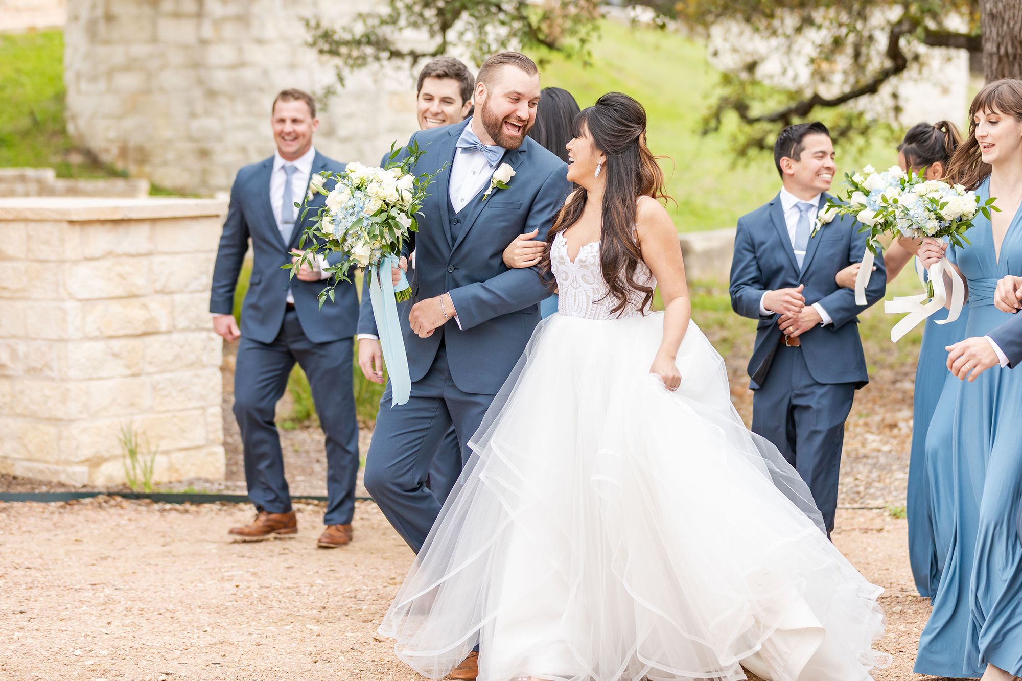 candid photo of a groom in a blue suit and bride walking together while smiling at each other