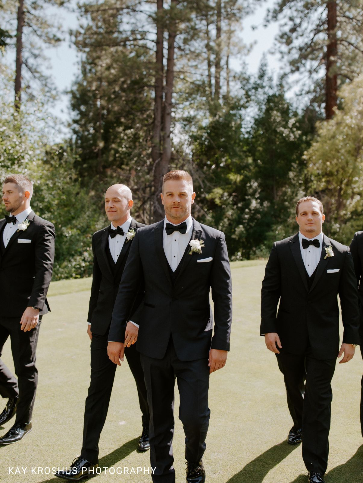 Groomsmen wearing matching black tuxedos with forest in the background