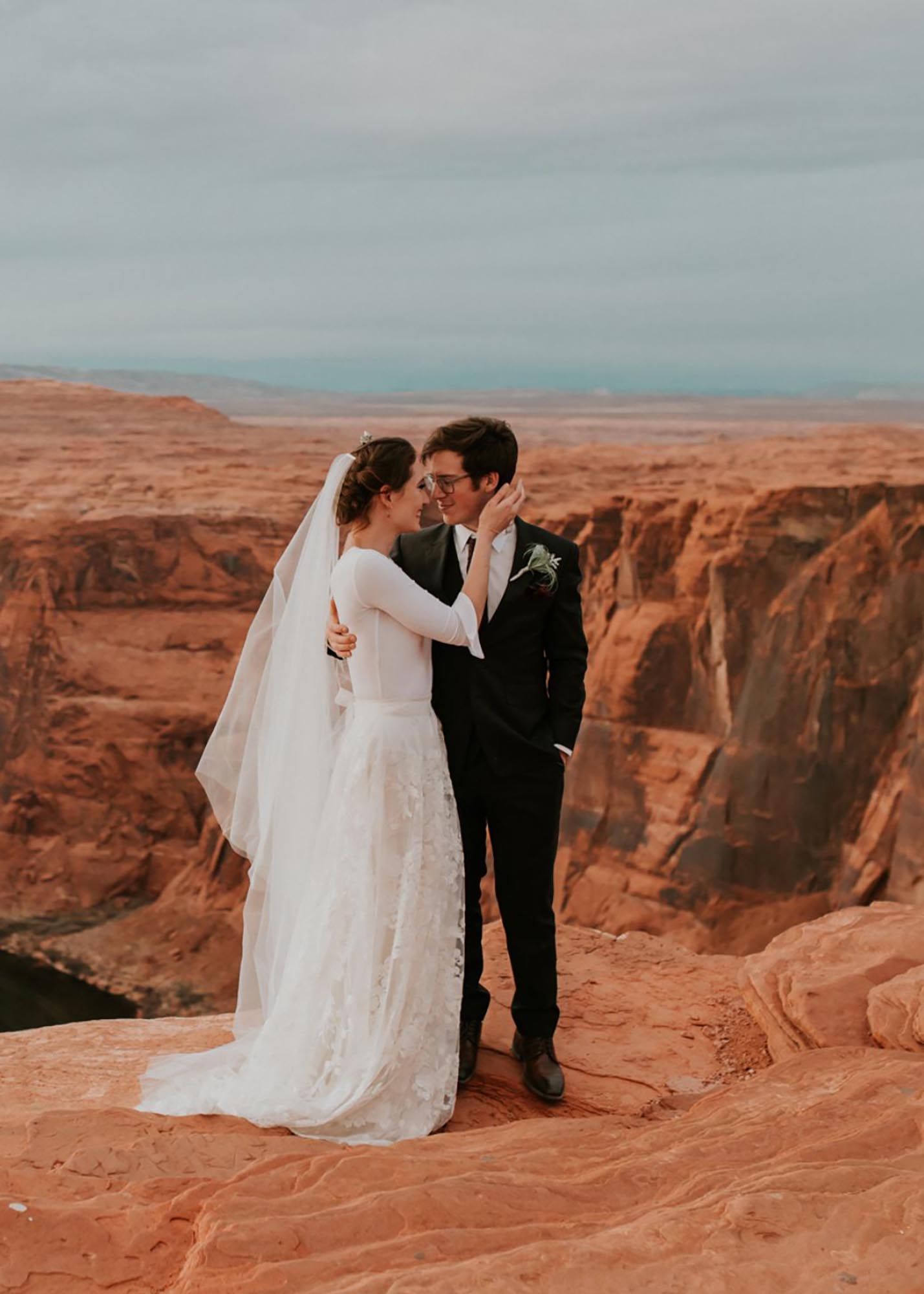 photo of a groom wearing a charcoal suit and bride wearing a wedding dress with the grand canyon in the background