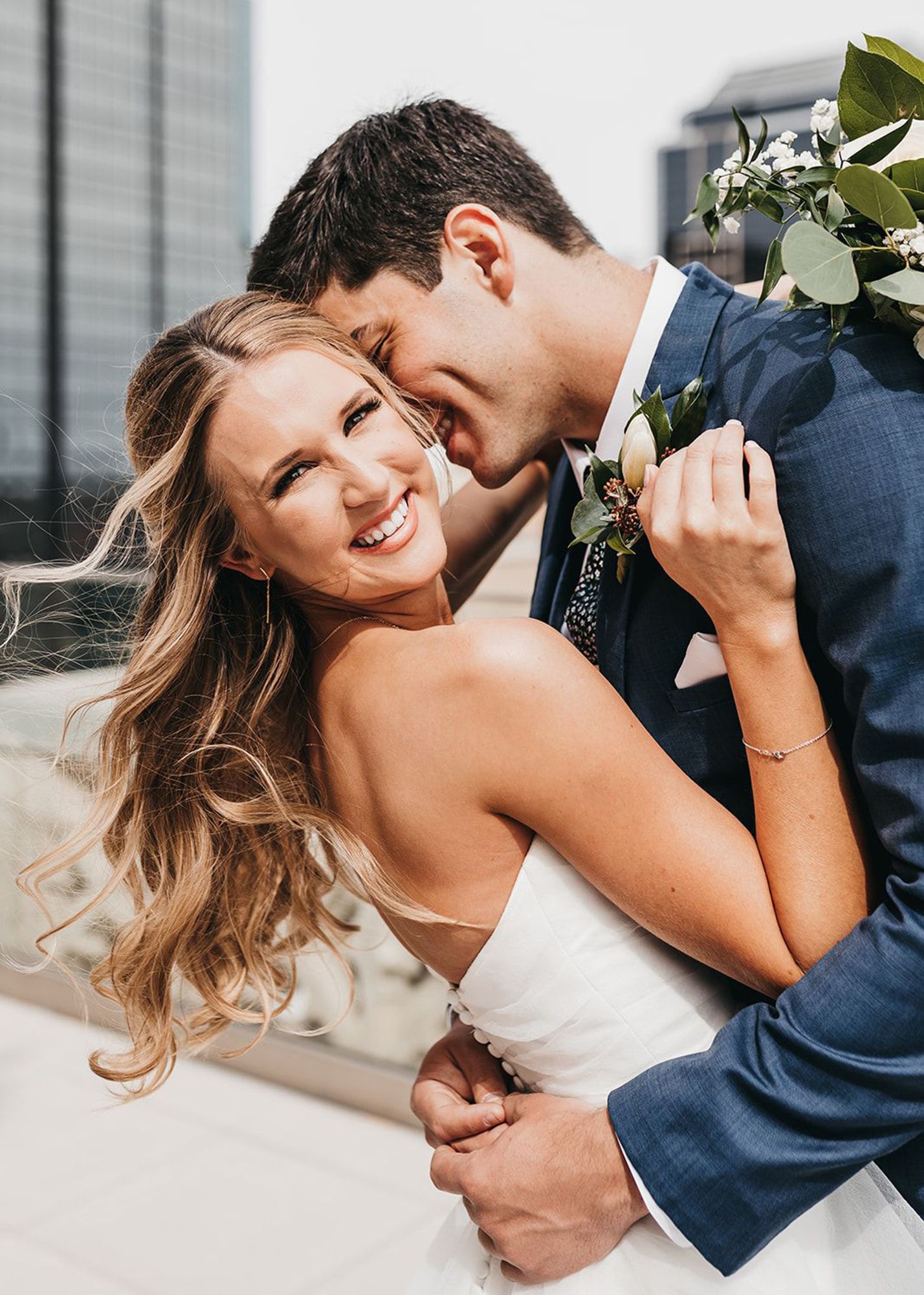 photo of groom in a blue suit and bride embracing during wedding while the bride smiles into the camera