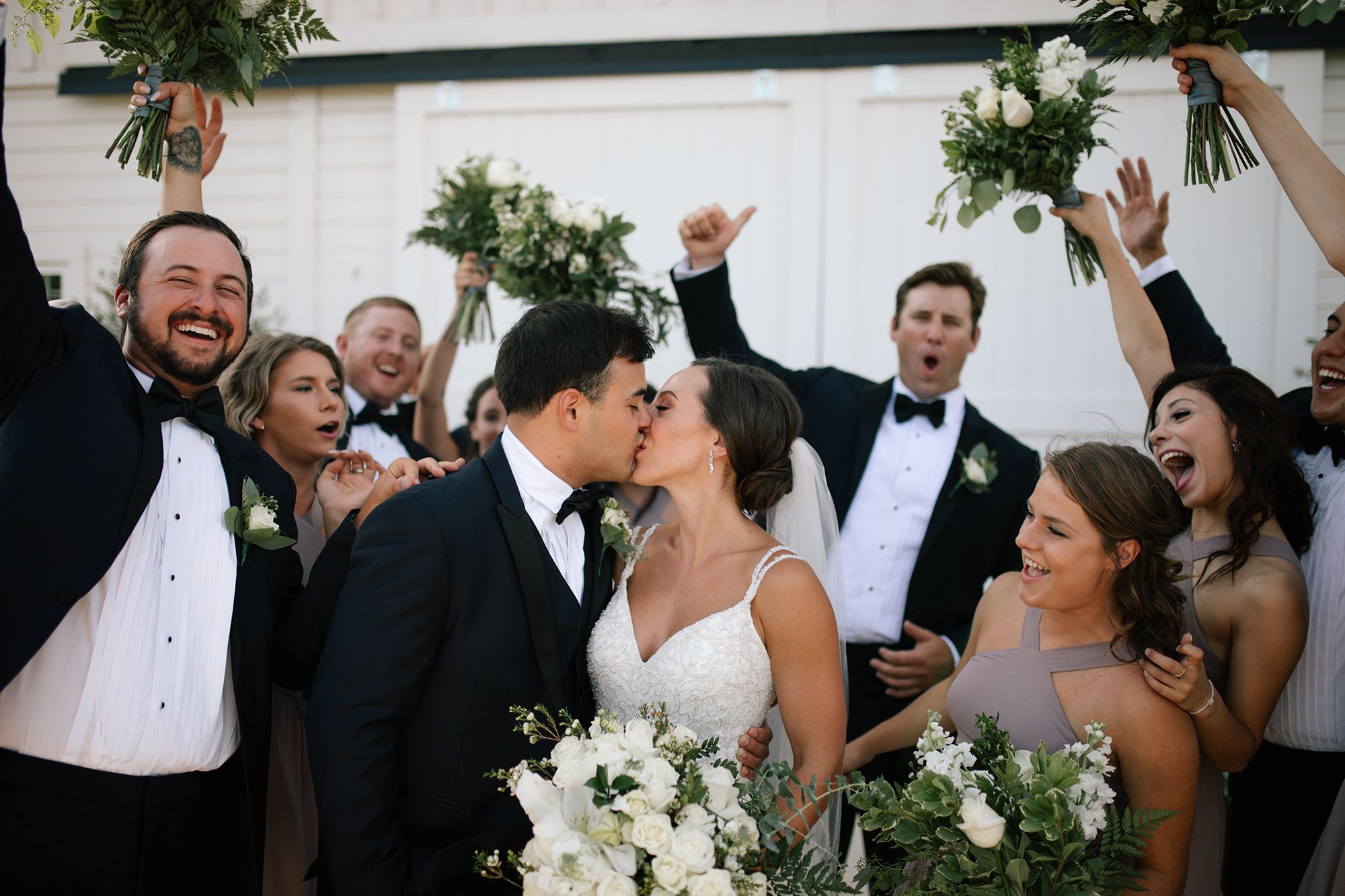 photo of groom in a black tuxedo and bride kissing during a wedding ceremony