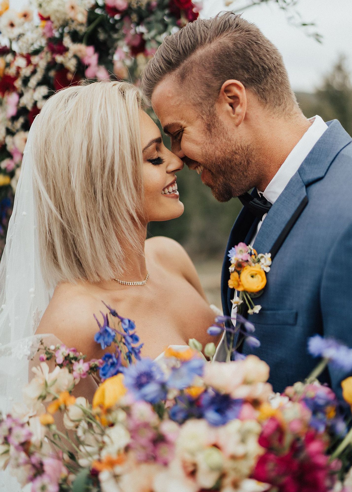 photo of a groom in a blue suit and bride during a wedding ceremony surrounded by flowers