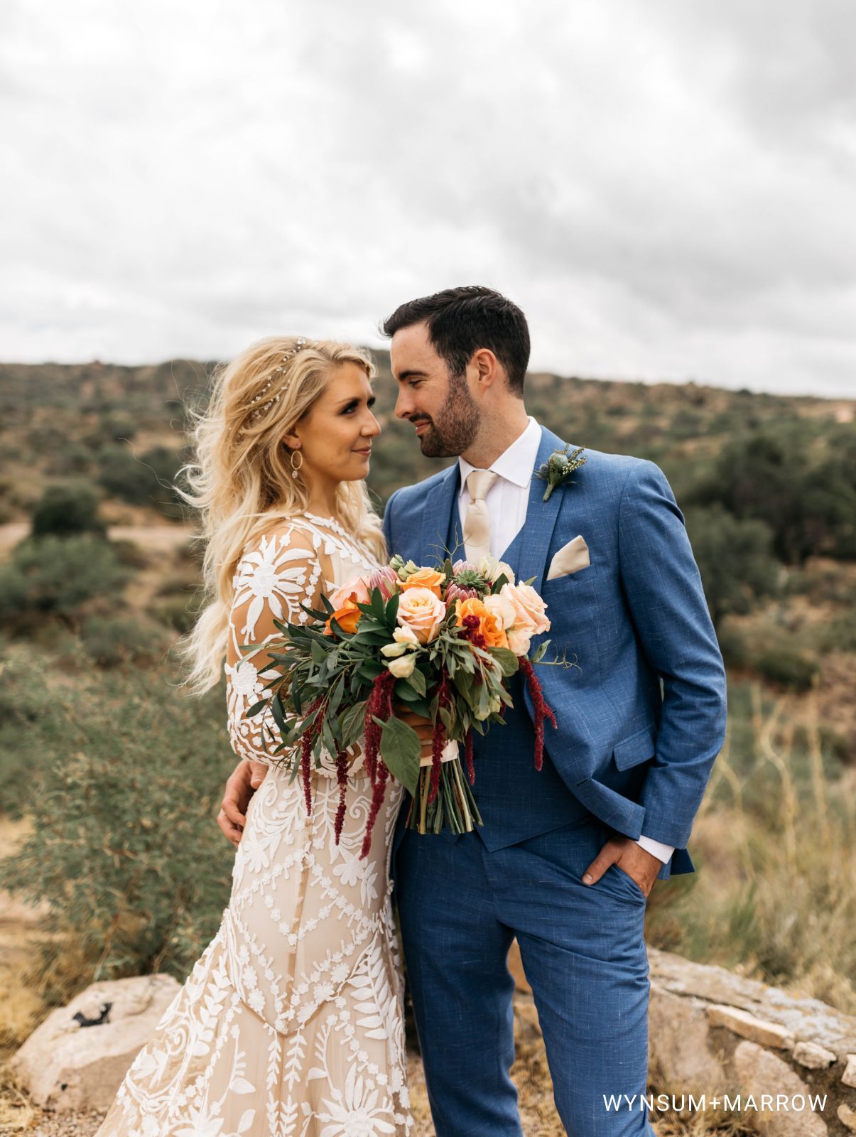 Bride and Groom in blue suit standing on a mountaintop