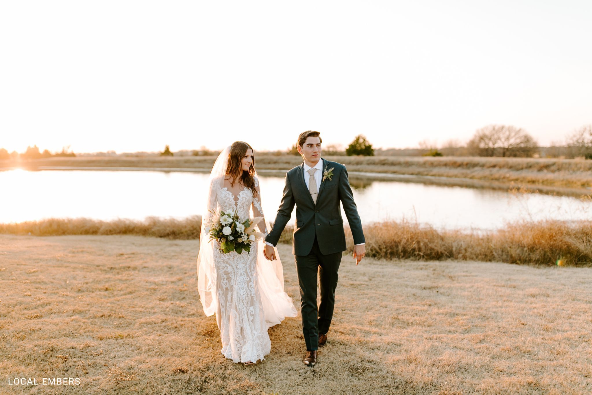 Groom wearing Generation Tux wedding suit in nature holding bride's hand.