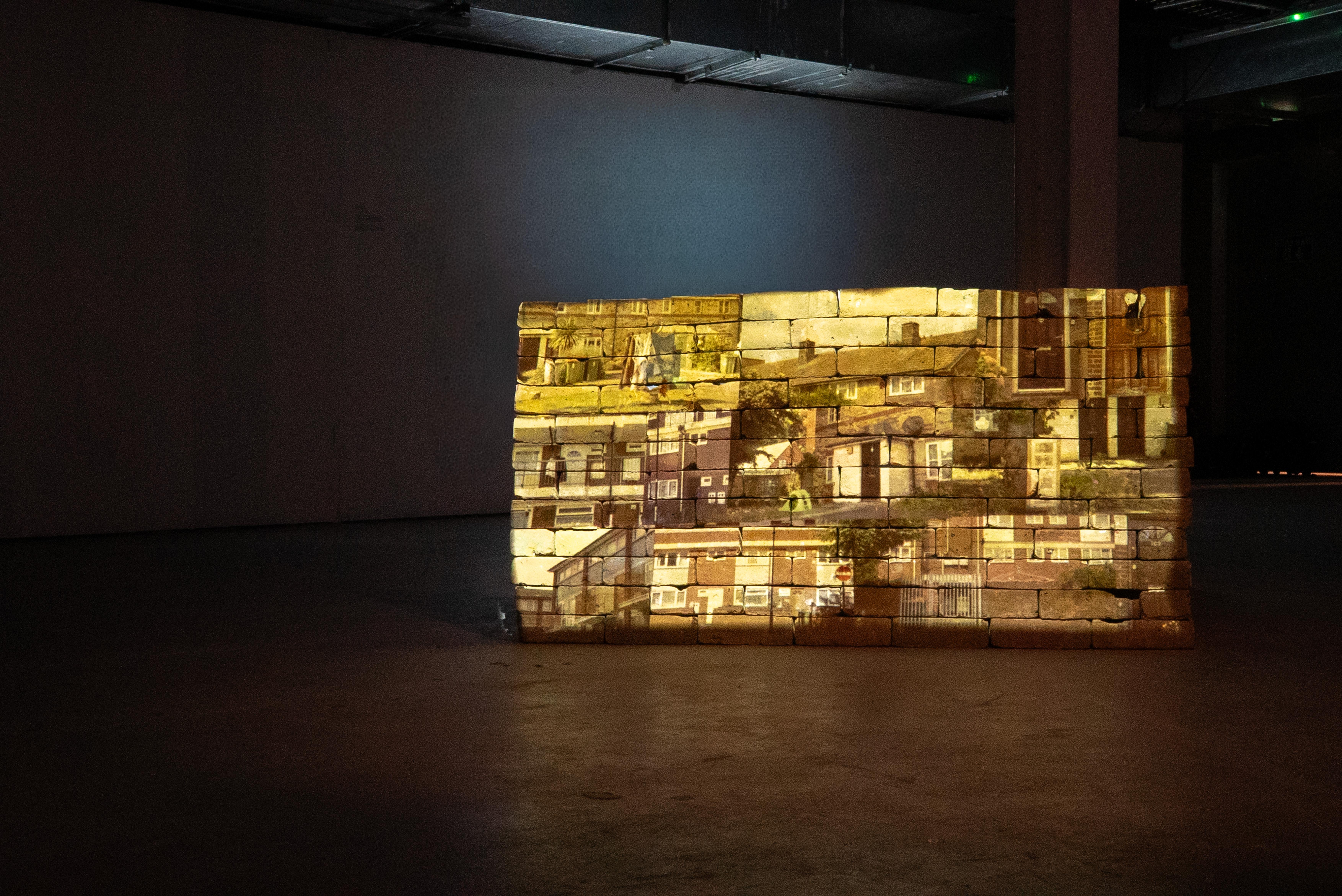 Video stills of the remaining buildings of the Custom House Estate projected onto a wall constructed from bricks salvaged from demolished sections of the estate.