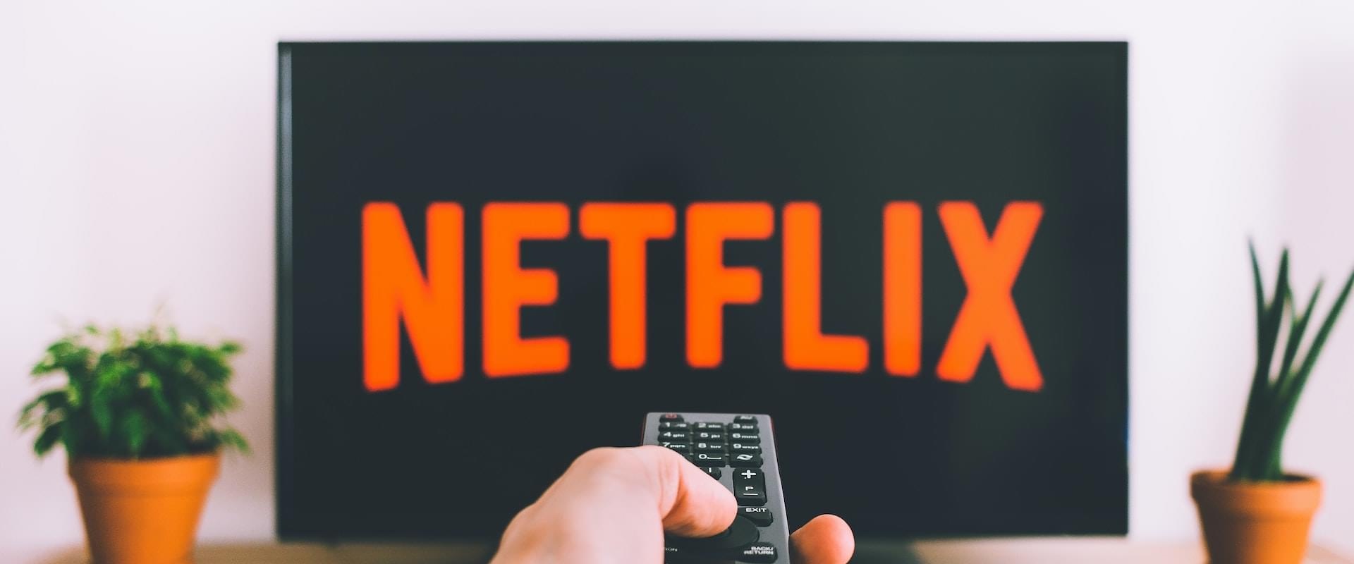 Hand with remote pointing at a TV displaying Netflix logo
