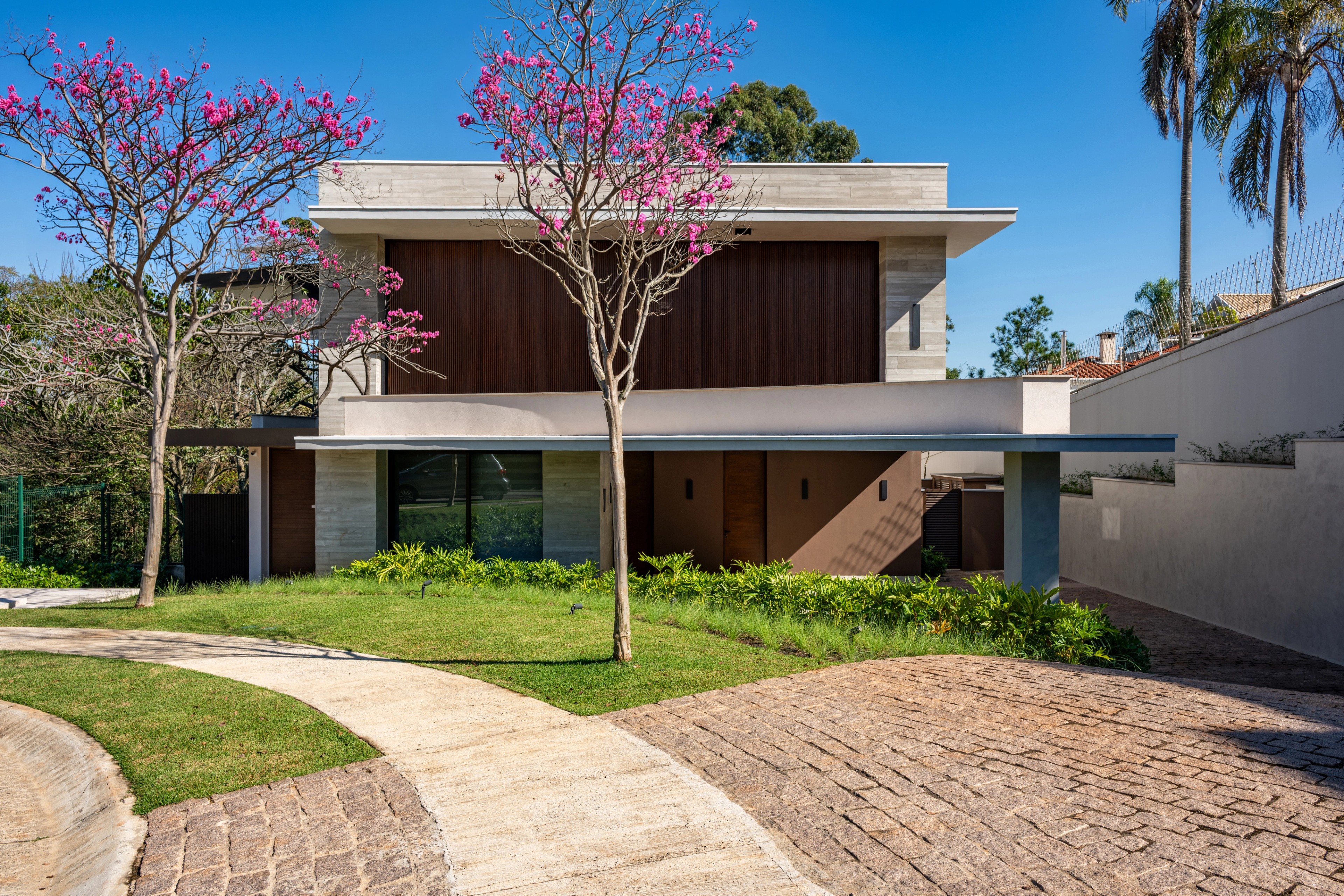 Residência SMI — Fachada frontal com acesso de pedestres, jardim e árvores floridas