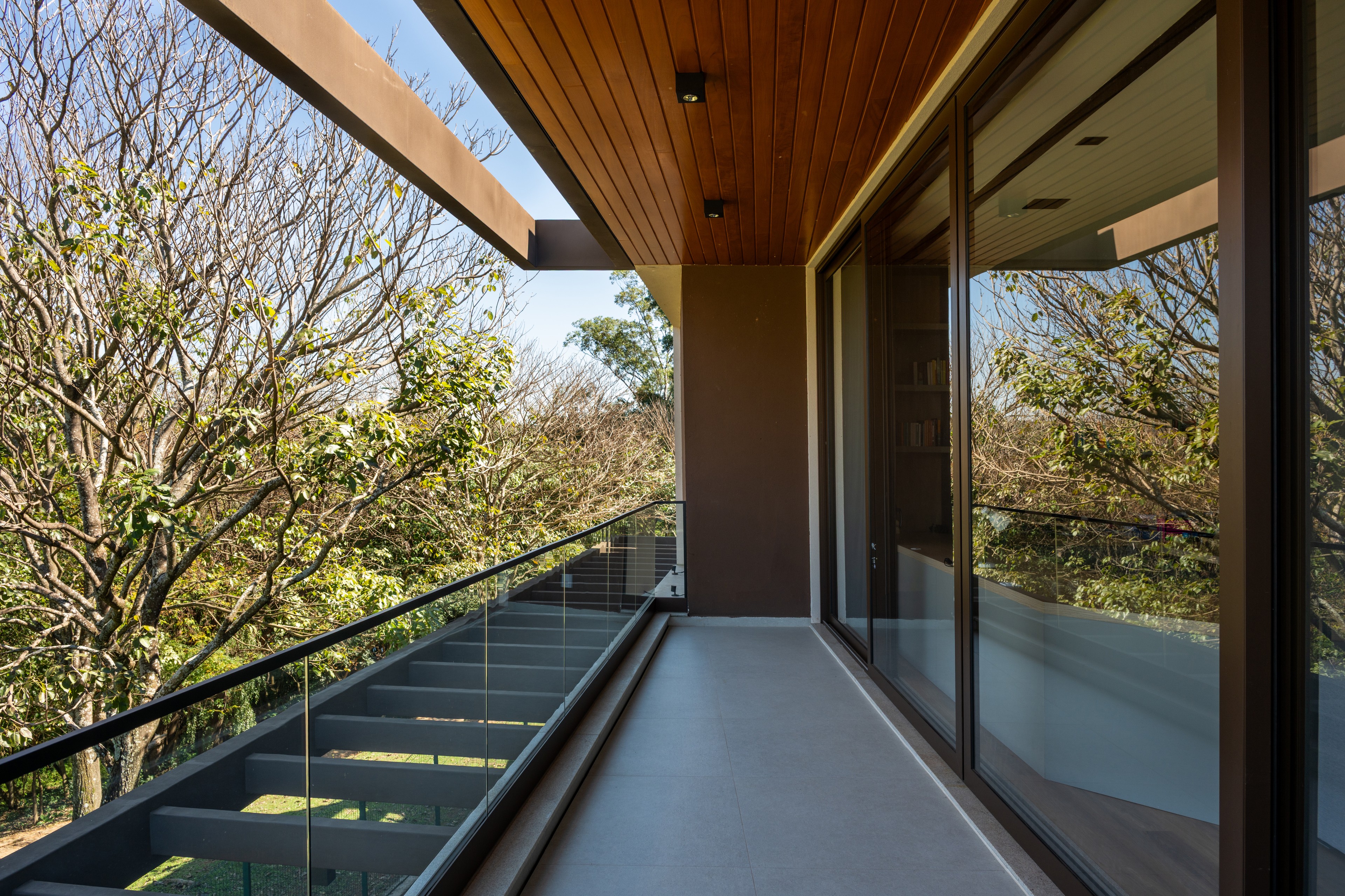 Residência SMI — Varanda superior com guarda-corpo de vidro e vista para as árvores