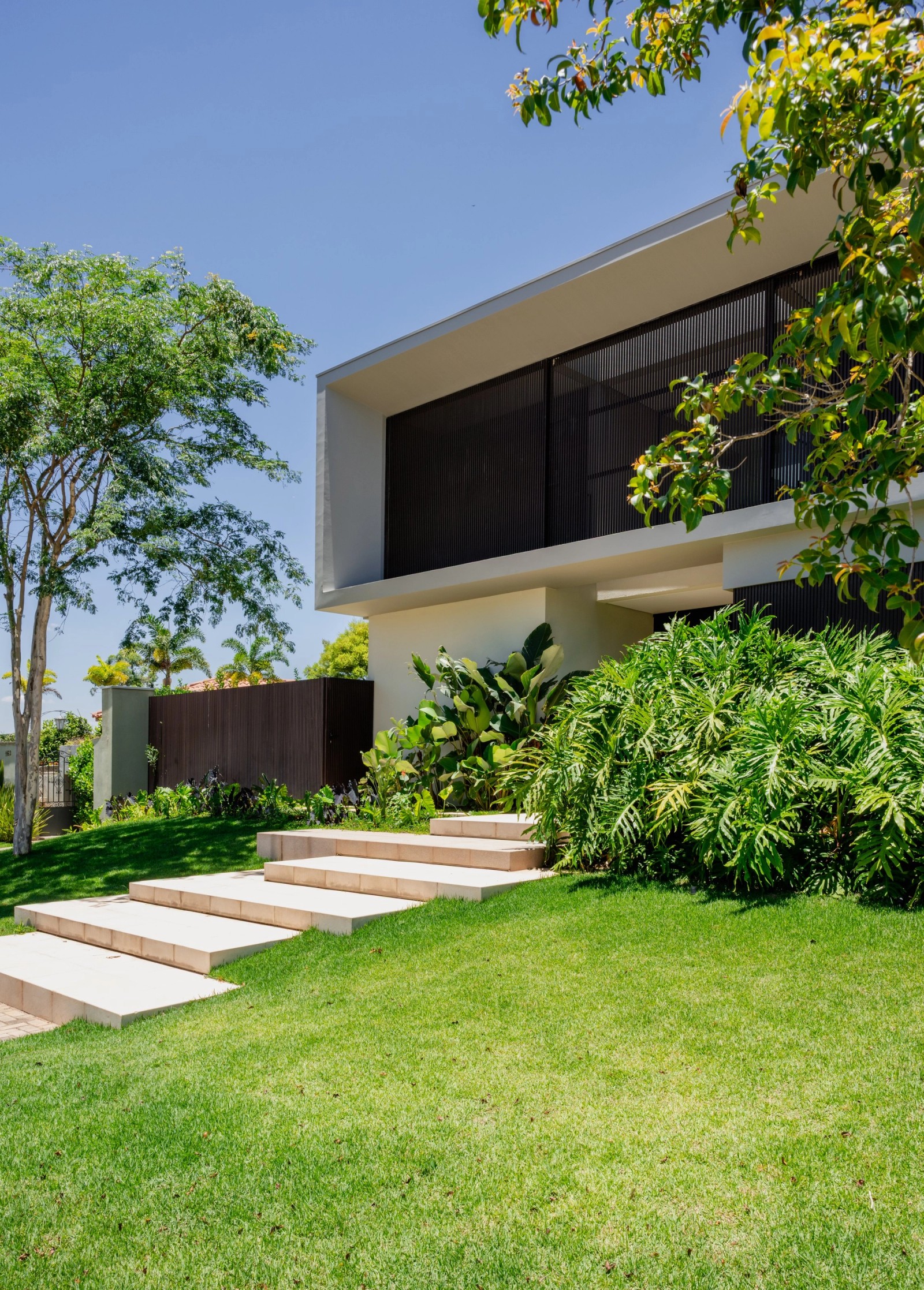 Residência MAN — Fachada frontal com brises, jardim e acesso em degraus