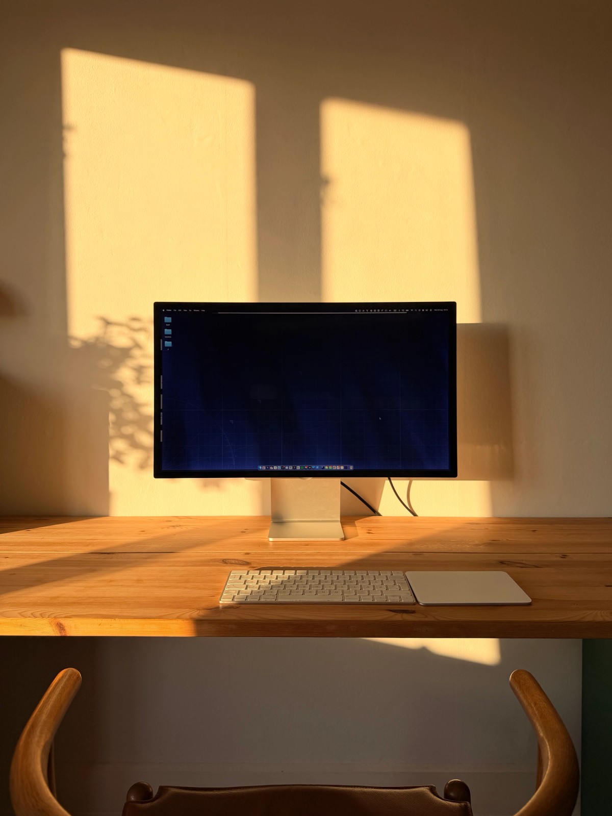 Close up of Apple Studio Display, Magic Keyboard, and Magic Trackpad against a sunlit wall.