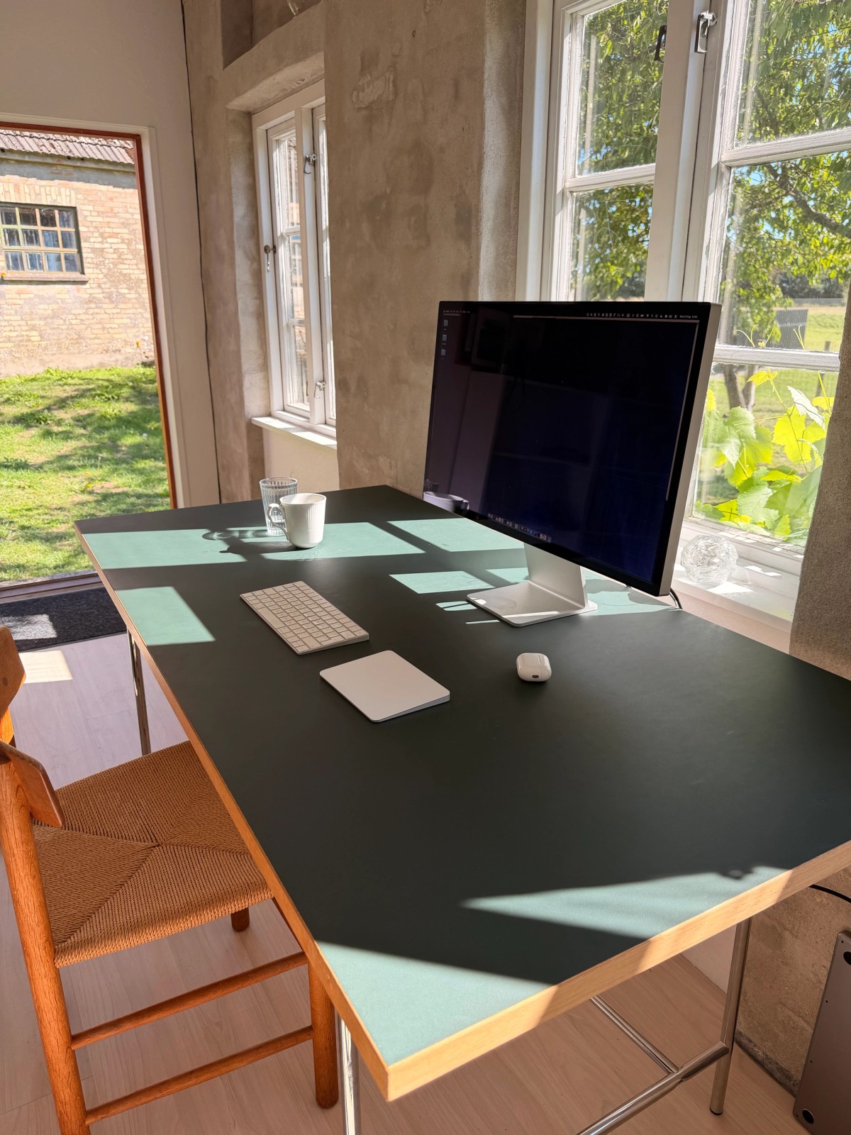 Eiermann desk with a dark linoleum top and an Apple Studio Display beside a sunlit window
