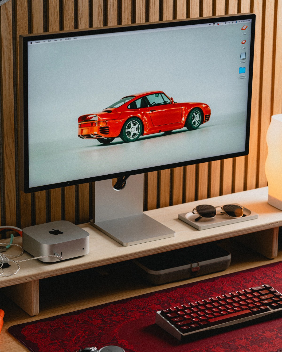 The desk with a red Porsche on the monitor, a dark red keyboard and a patterned red deskpad.