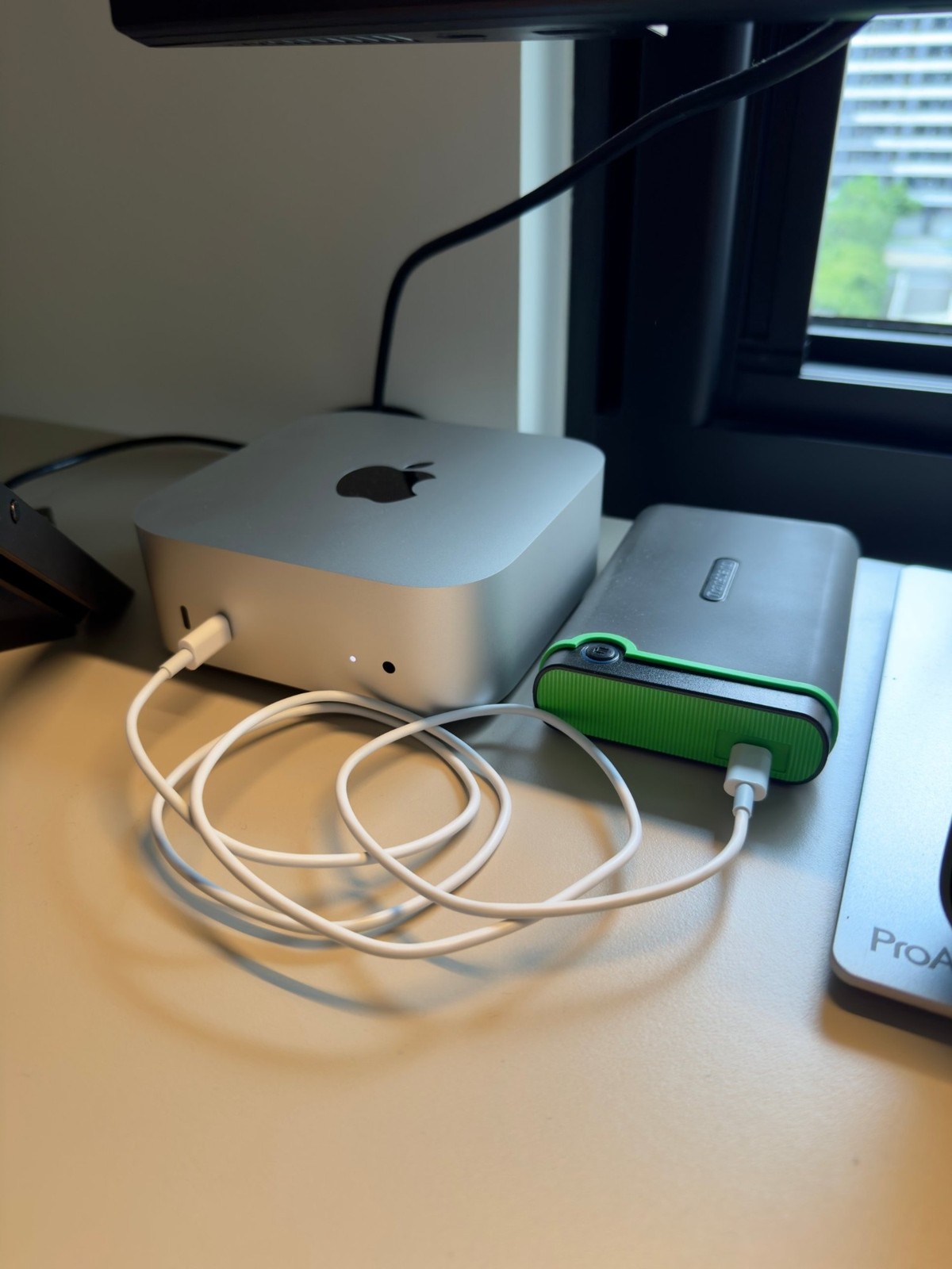 A Mac mini beside a green Transcend portable drive on the desk, with a coiled white cable in front of them.