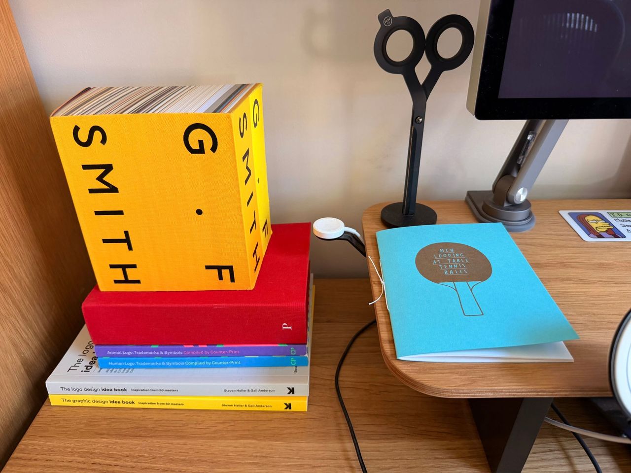 A stack of design books including a GF Smith paper sample book and the Pentagram Marks book, beside black magnetic scissors and a blue zine.