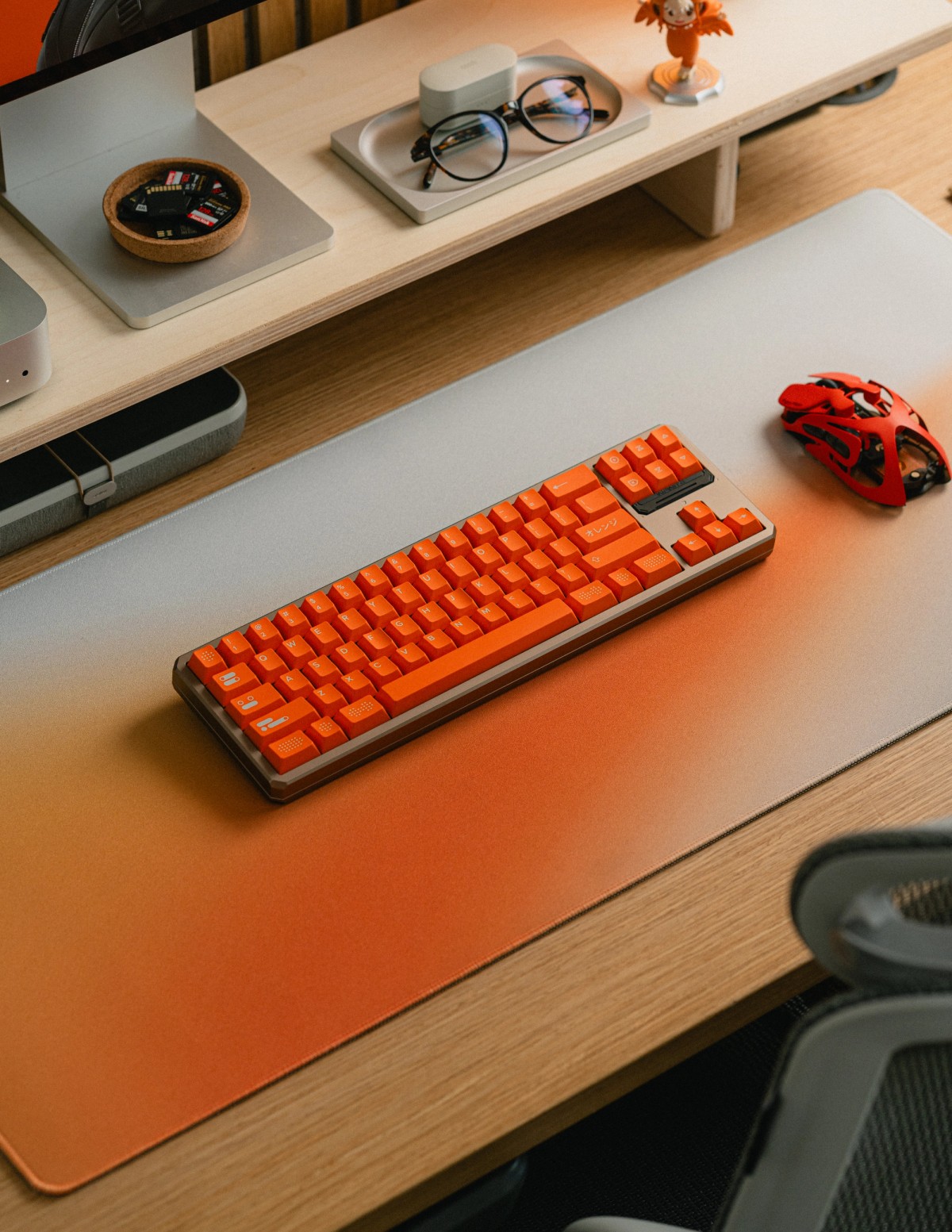 Looking along the desk at an orange mechanical keyboard on a gray-to-orange gradient deskpad.