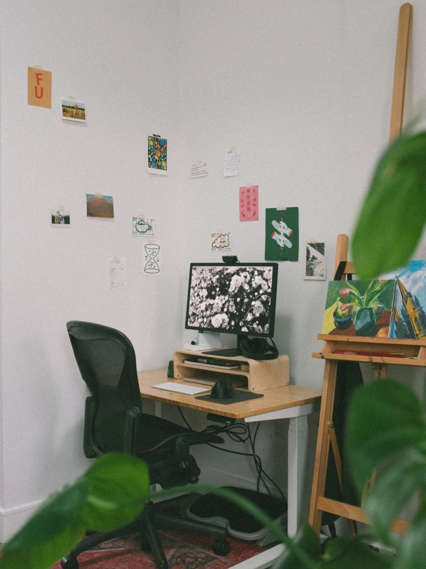 Jenny Wen’s workspace: a bamboo Jarvis desk with a wooden monitor riser, a black Herman Miller Aeron pulled up to it, and prints taped to the wall.