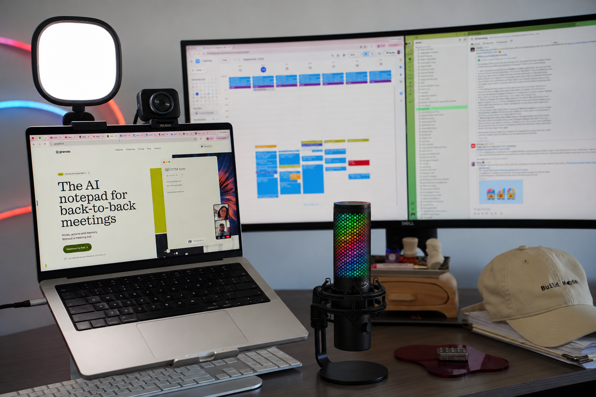 MacBook Pro on a laptop stand showing the Granola website, an LED panel light and webcam clipped above the screen, and a Dell ultrawide behind