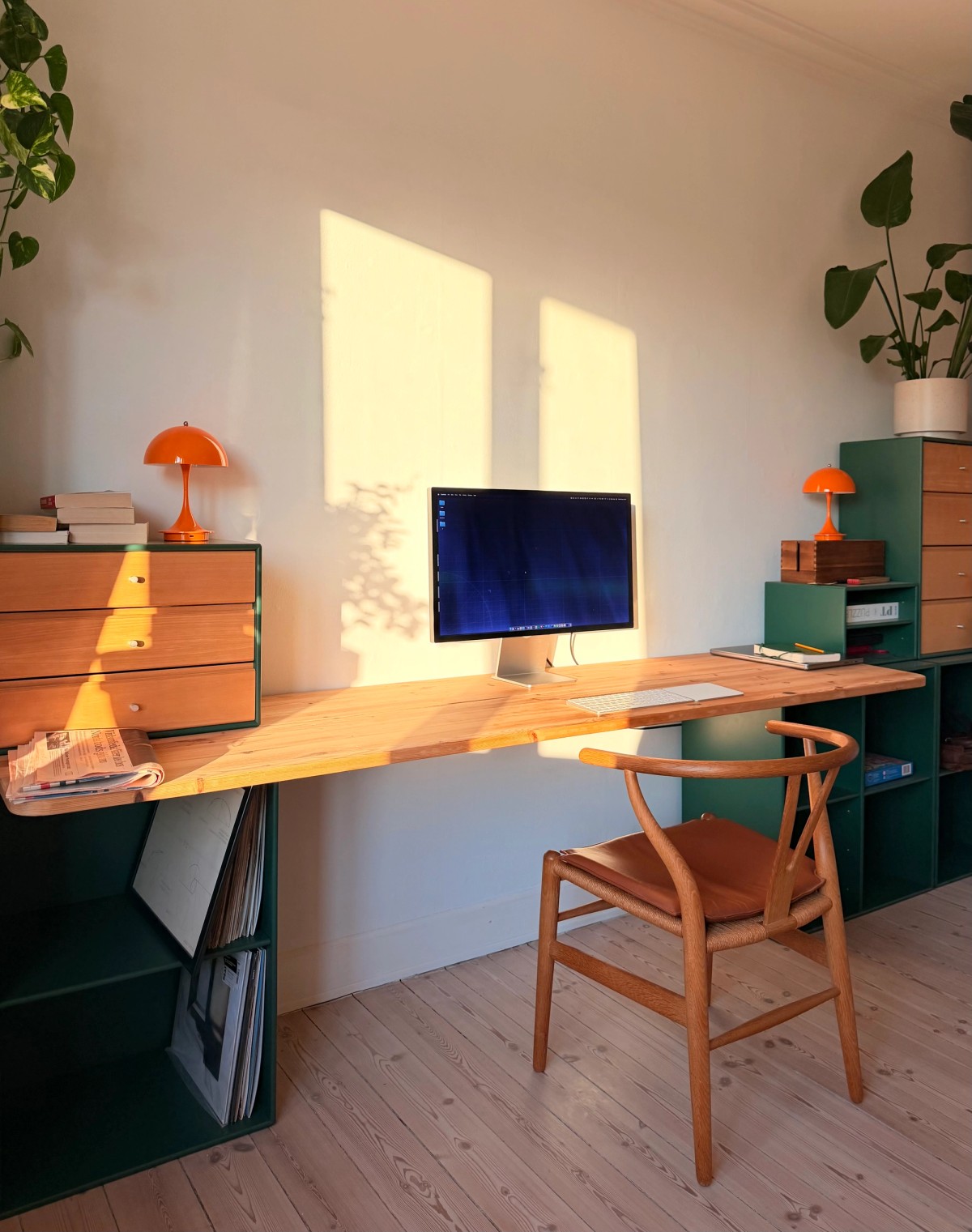 Apple Studio Display on a pine desk with Magic Keyboard and Trackpad, evening sun casting window shapes on the wall