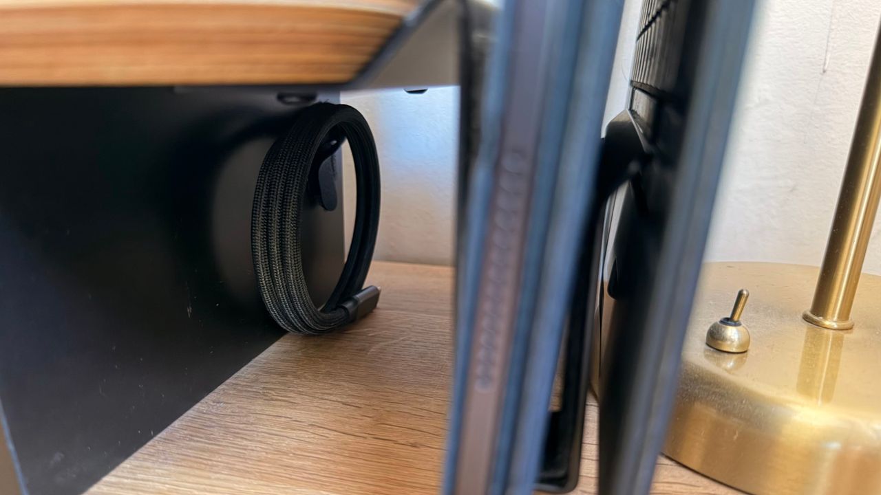 A magnetic Thunderbolt cable coiled and tucked down the far side of the desk shelf, out of sight.