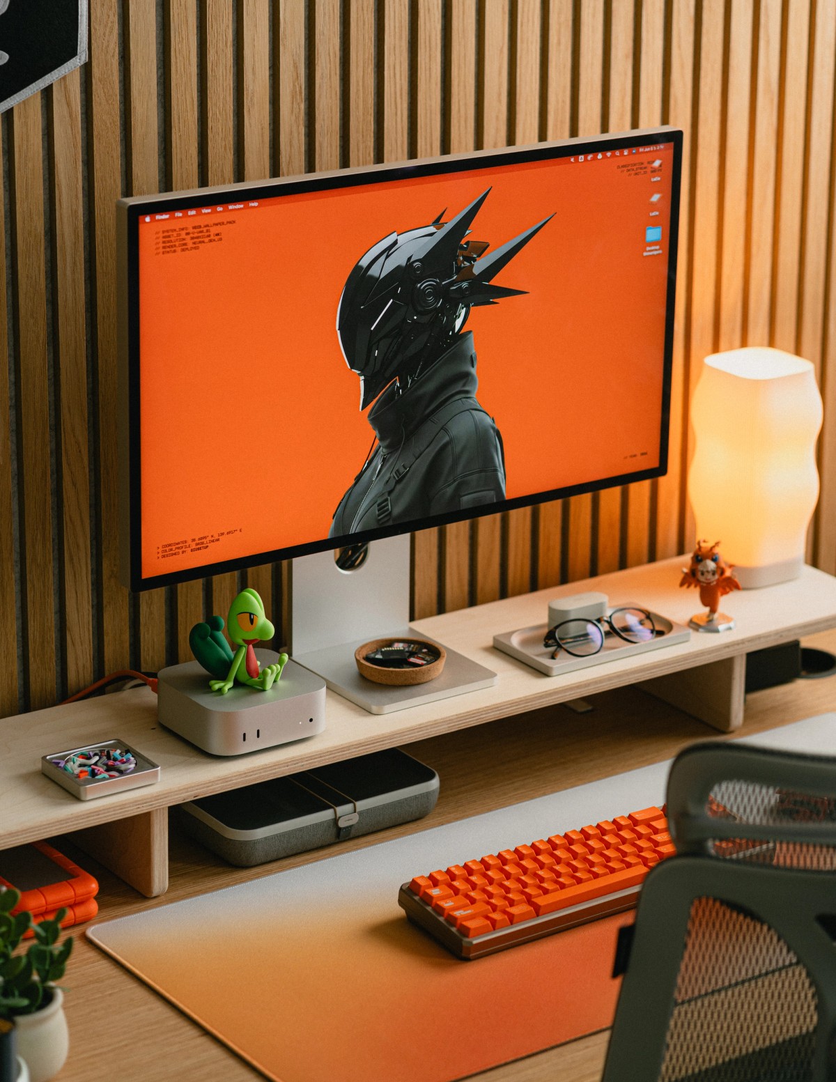 An angled view of the desk: a monitor showing an orange cyberpunk illustration, a Treecko figure on a Mac Mini, and an orange mechanical keyboard below.