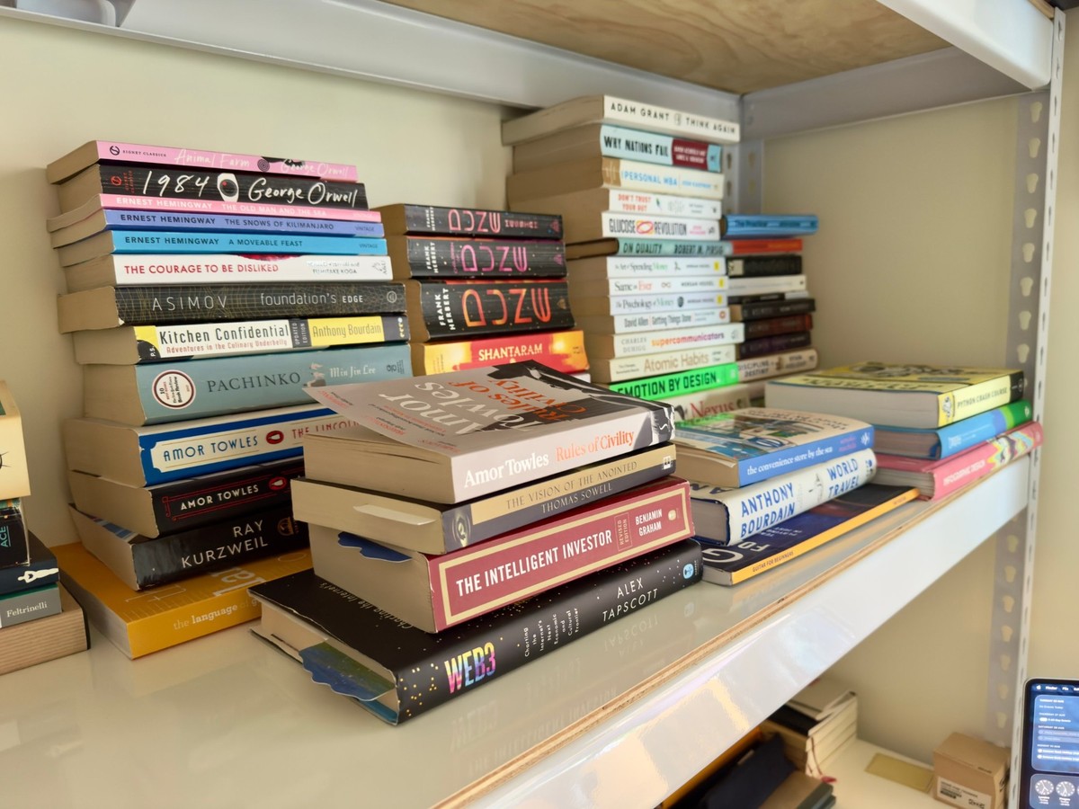 Stacks of books on a white shelf, including Orwell, Hemingway, Dune, Amor Towles, The Intelligent Investor and Python Crash Course.
