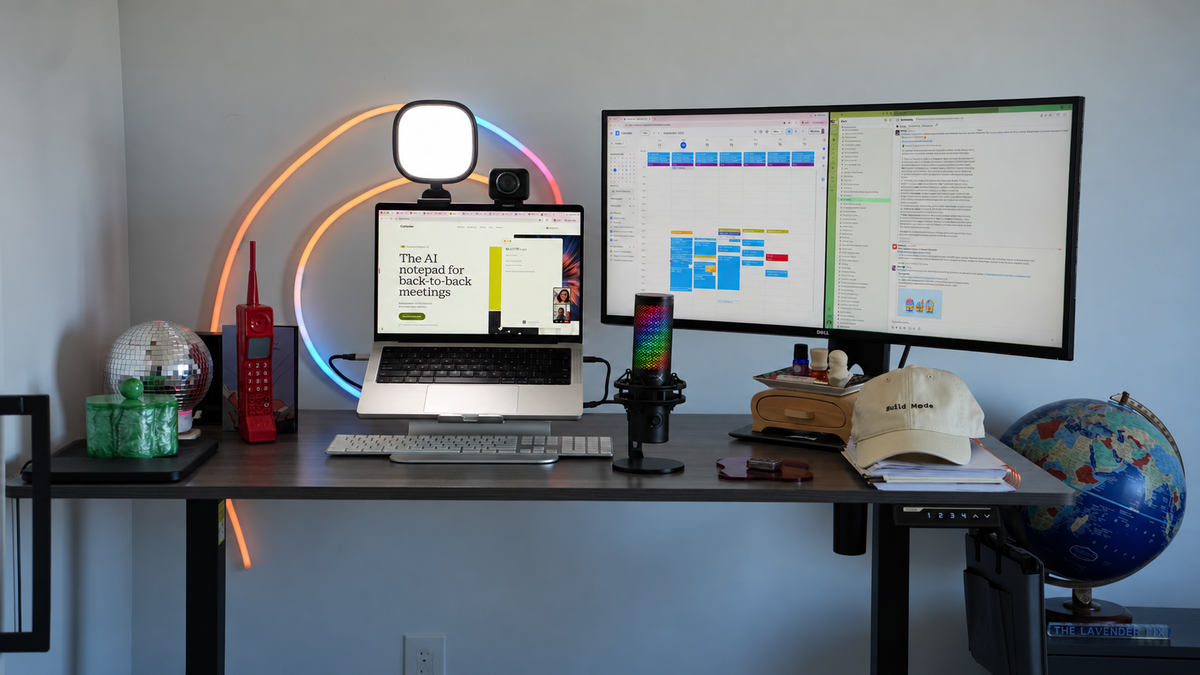 Home office desk with a MacBook Pro on a stand, a Dell curved ultrawide monitor, a HyperX microphone and a neon rope light coiled in a spiral on the wall behind