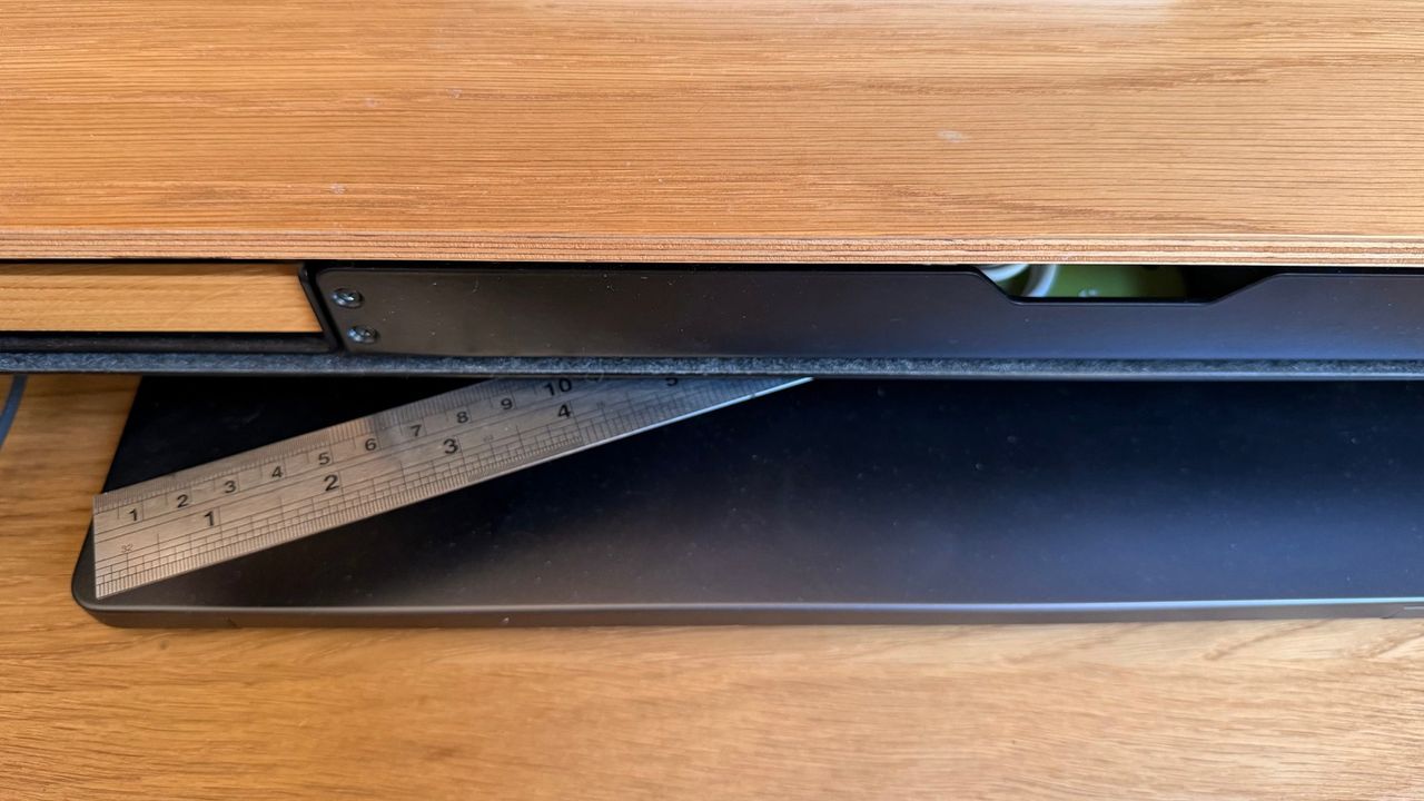 A steel ruler held by a magnet under the edge of the desk shelf, above the keyboard tray.