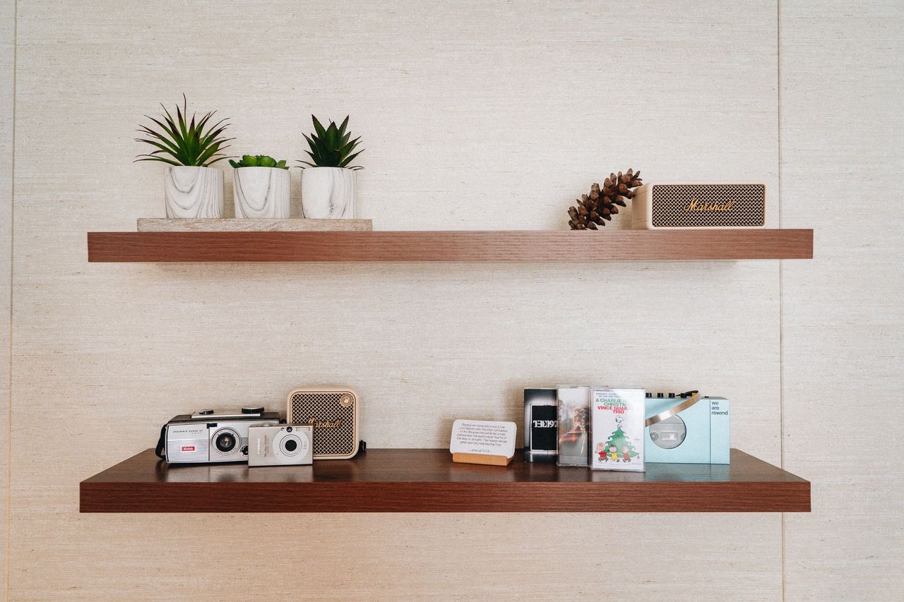 Two floating wooden shelves holding small succulents, a Marshall speaker and compact cameras
