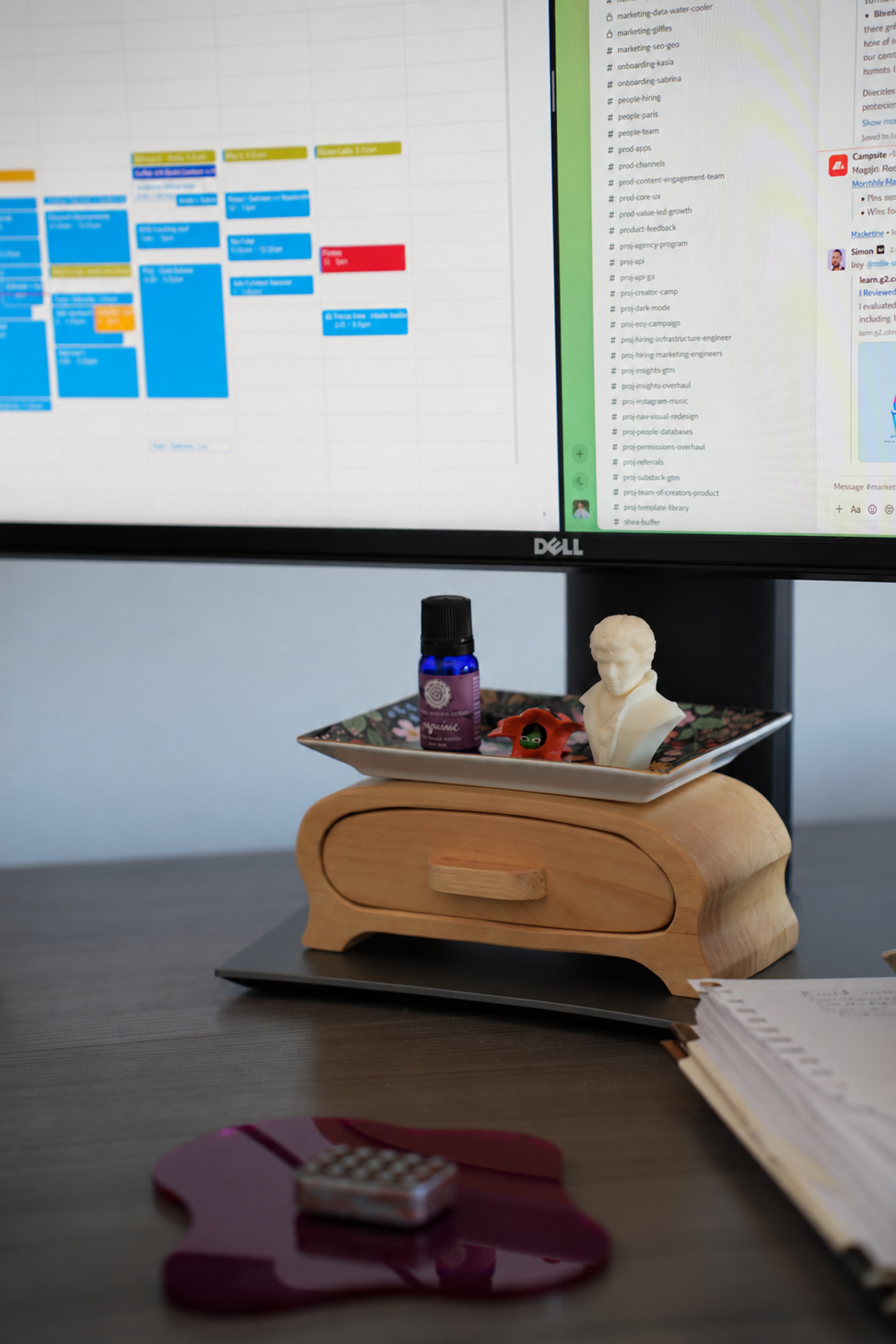 Slack channels on the Dell ultrawide above a wooden keepsake box holding a floral tray, an essential oil bottle and a small white bust