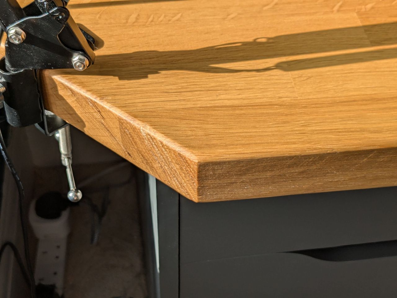 A close view of the oak worktop’s cut-away corner, with a drum stand clamped just beyond it.