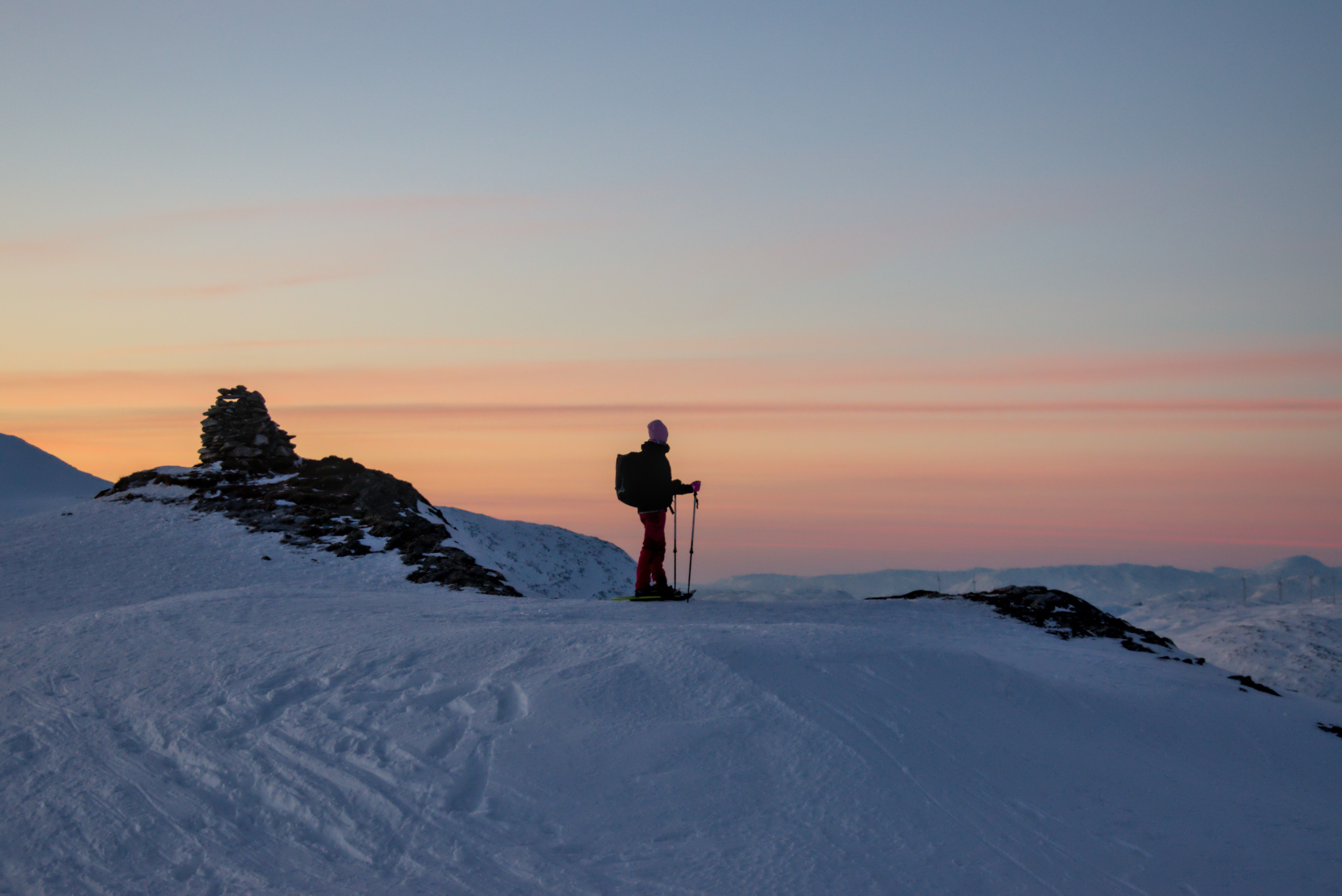 Snowshoeing in Tromsø: a person with poles on a snowy ridge beneath a pink and orange winter sky.