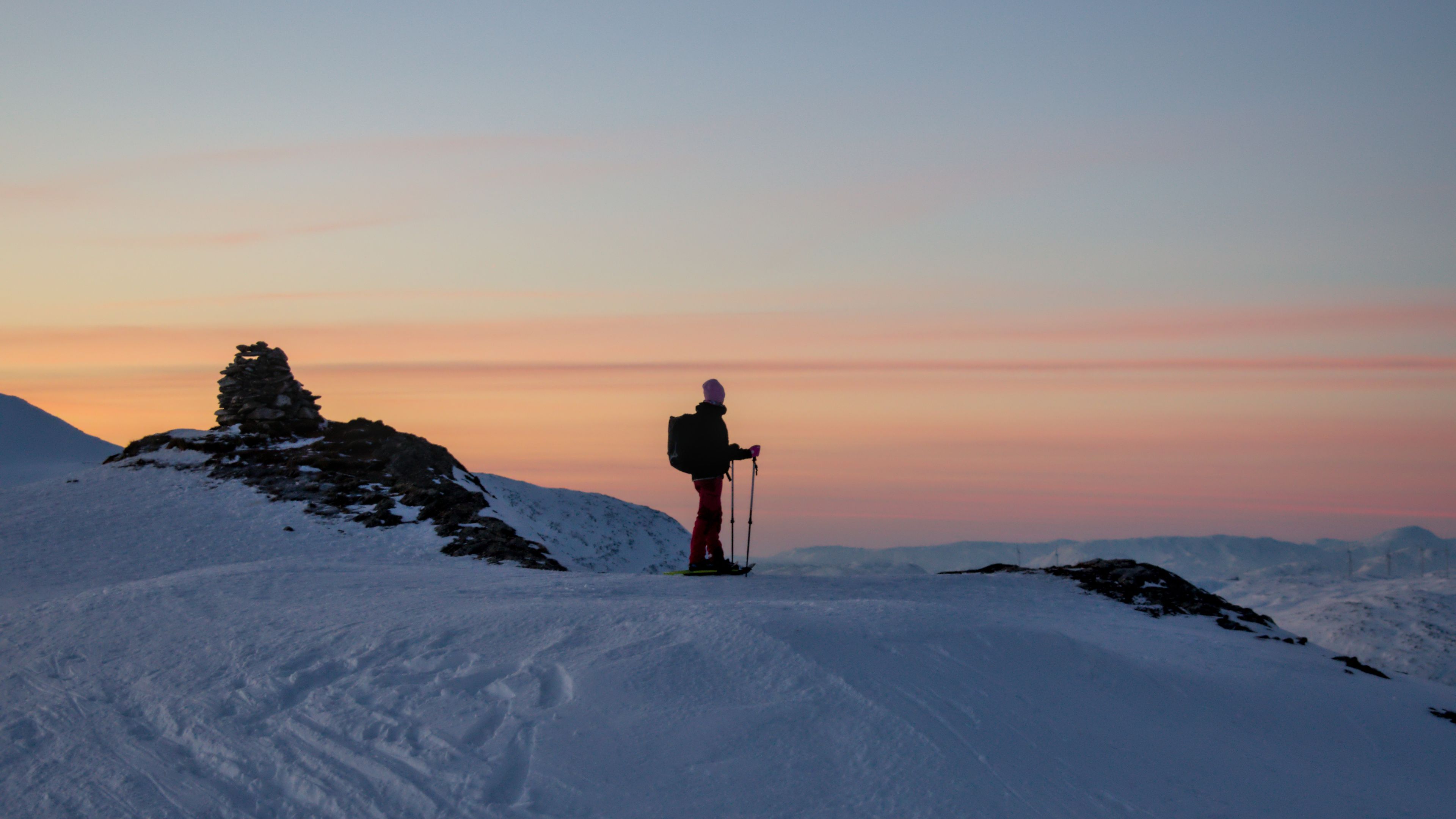 Snowshoeing in Tromsø: a person with poles on a snowy ridge beneath a pink and orange winter sky.