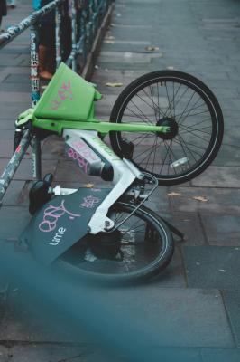 A green Lime e-bike lying on its side against a railing on a city pavement
