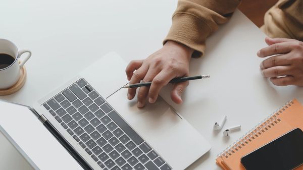 Person Holding Black Pen While Using Laptop