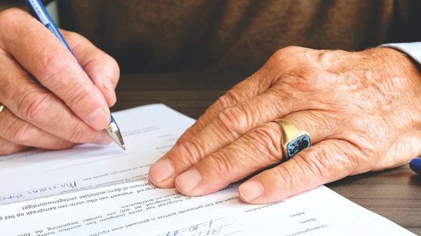 A wrinkled hand filling out paperwork