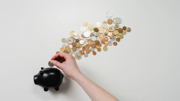 Image of hand inserting coin in piggy bank 