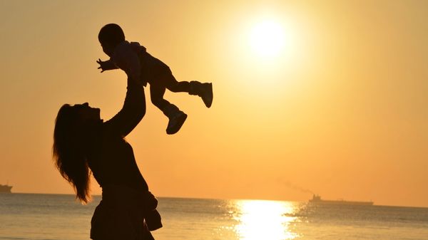 Woman Carrying Baby at Beach during Sunset