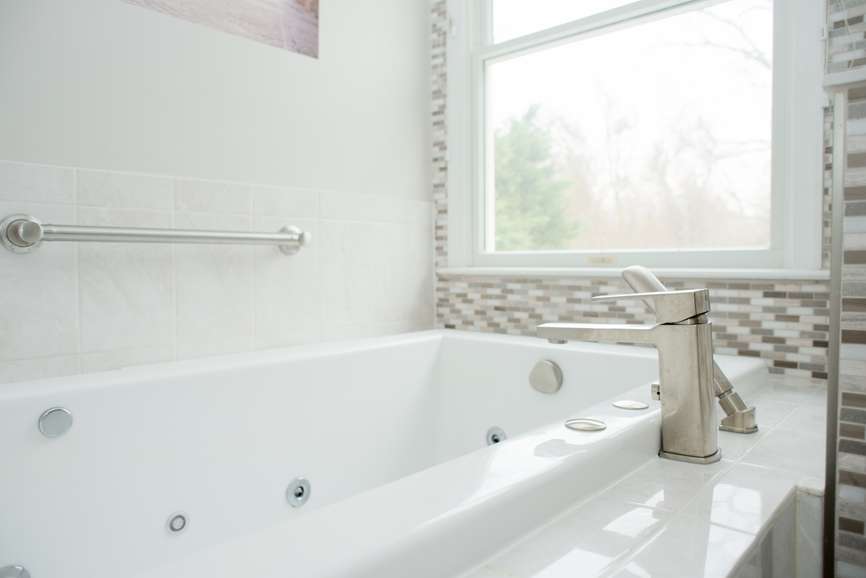 Sleek modern master bath renovation with stainless steel fixtures and a deep soaking jacuzzi tub in front of bright window