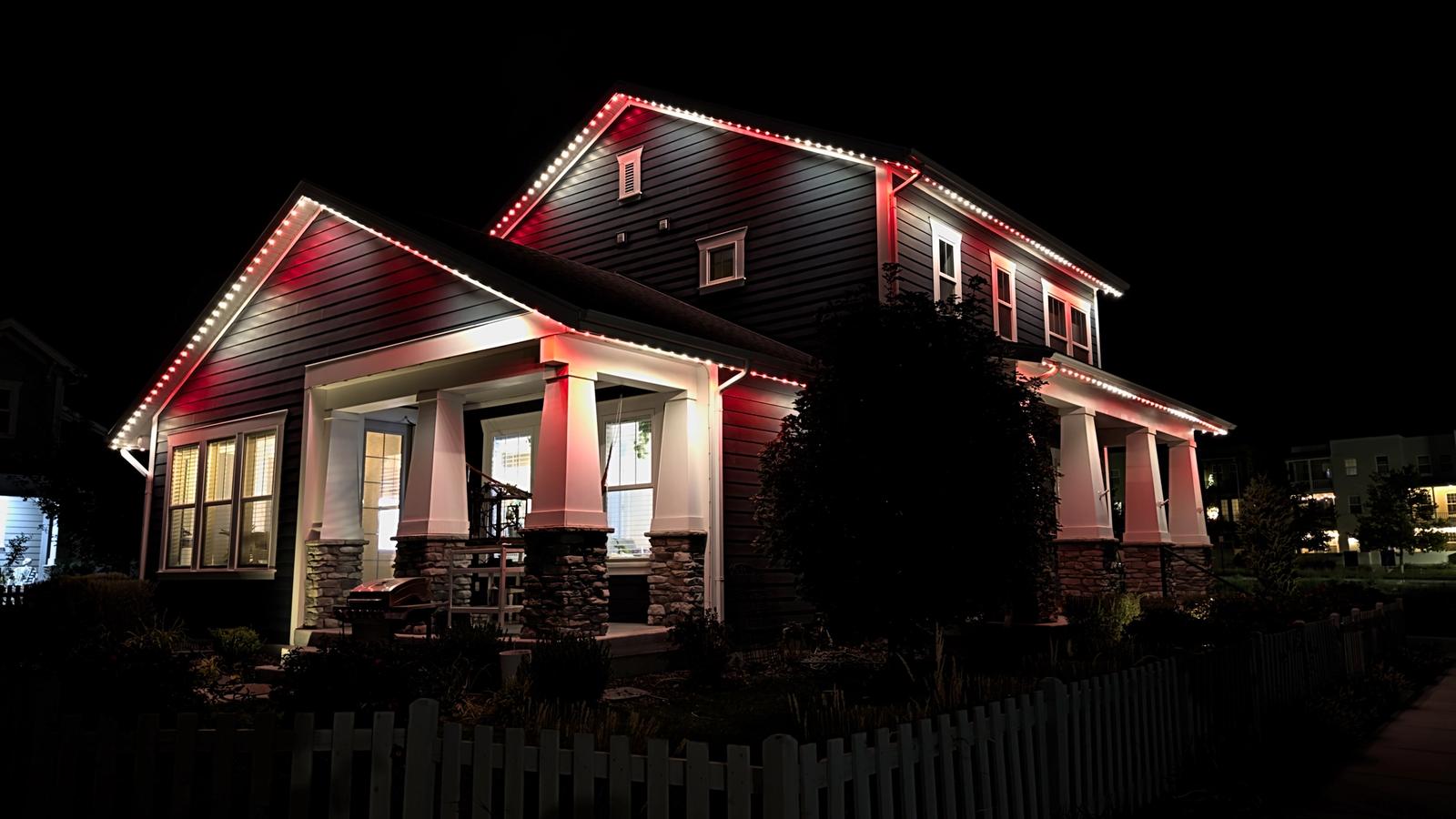 Two-story Utah home illuminated with red and warm white permanent outdoor Christmas lights along the rooflines and eaves at night.