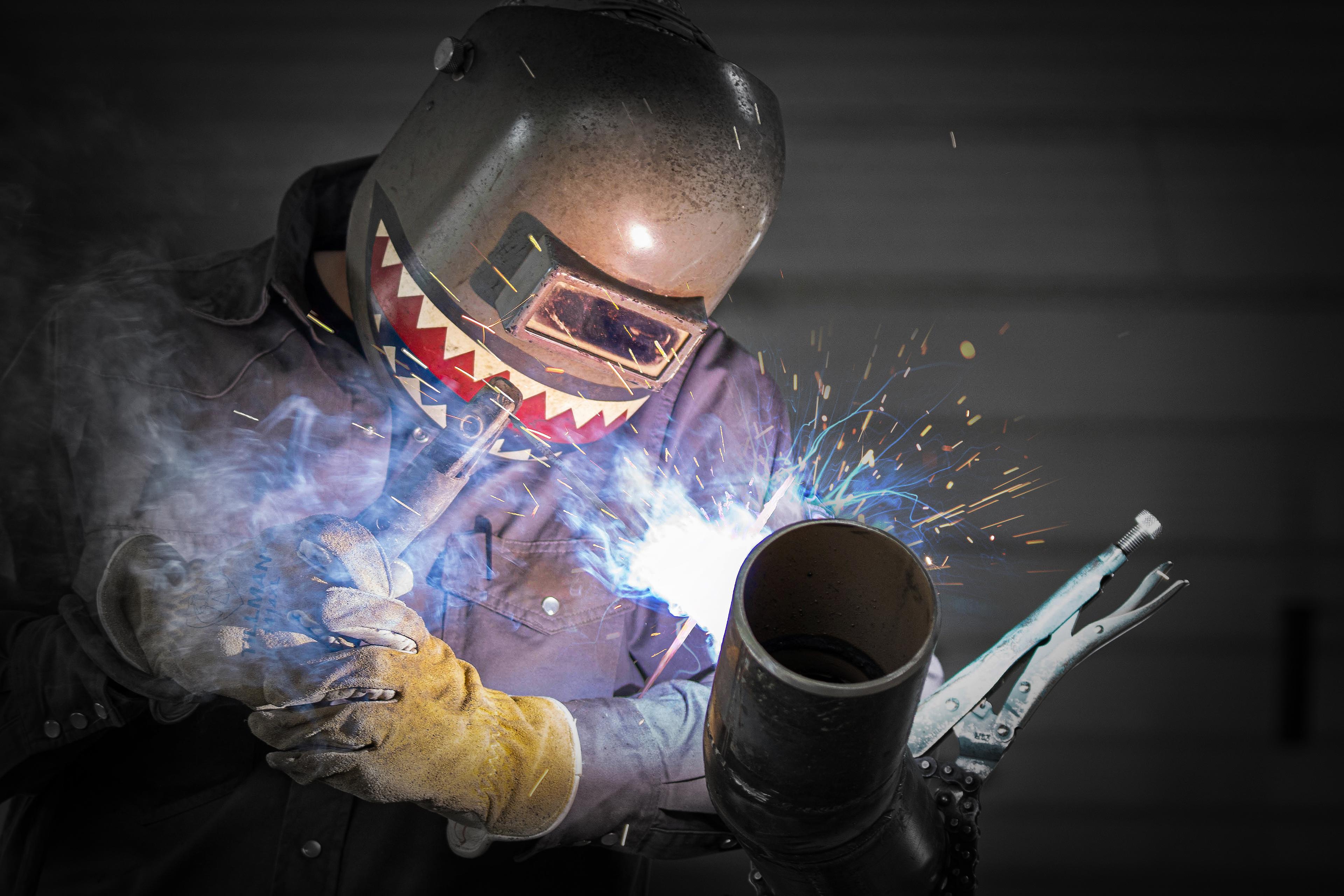 a construction worker welding while wearing a welding helmet that has a shark painted on it
