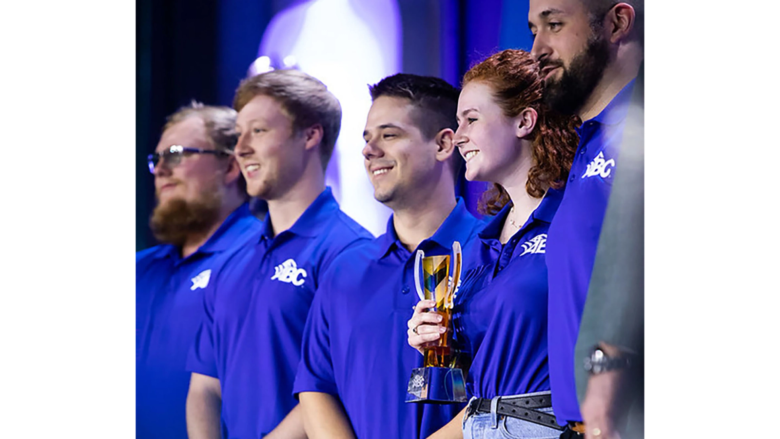 a young woman stands on stage holding an award surrounded by young men