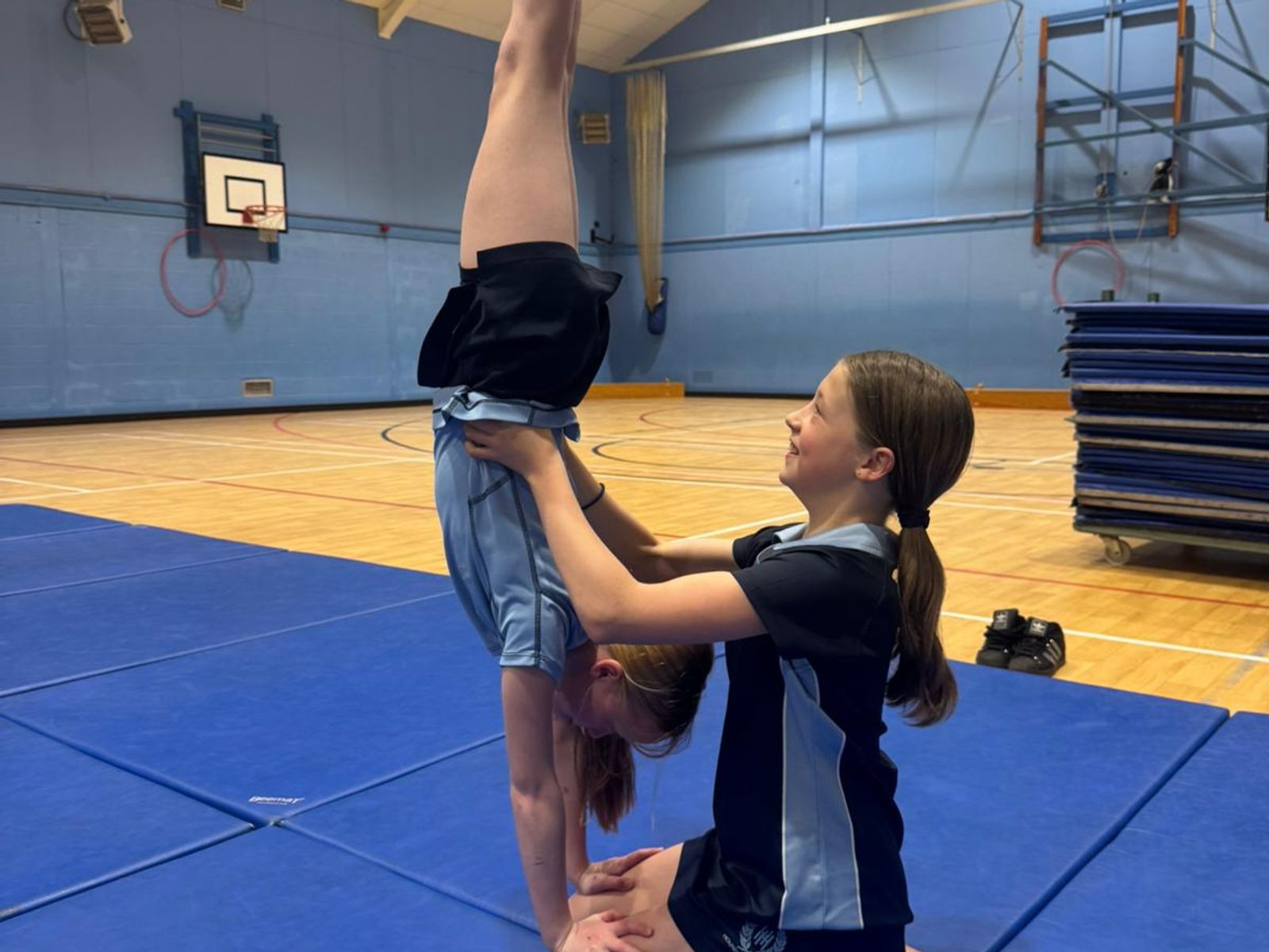 A coach supporting a young gymnast in a handstand